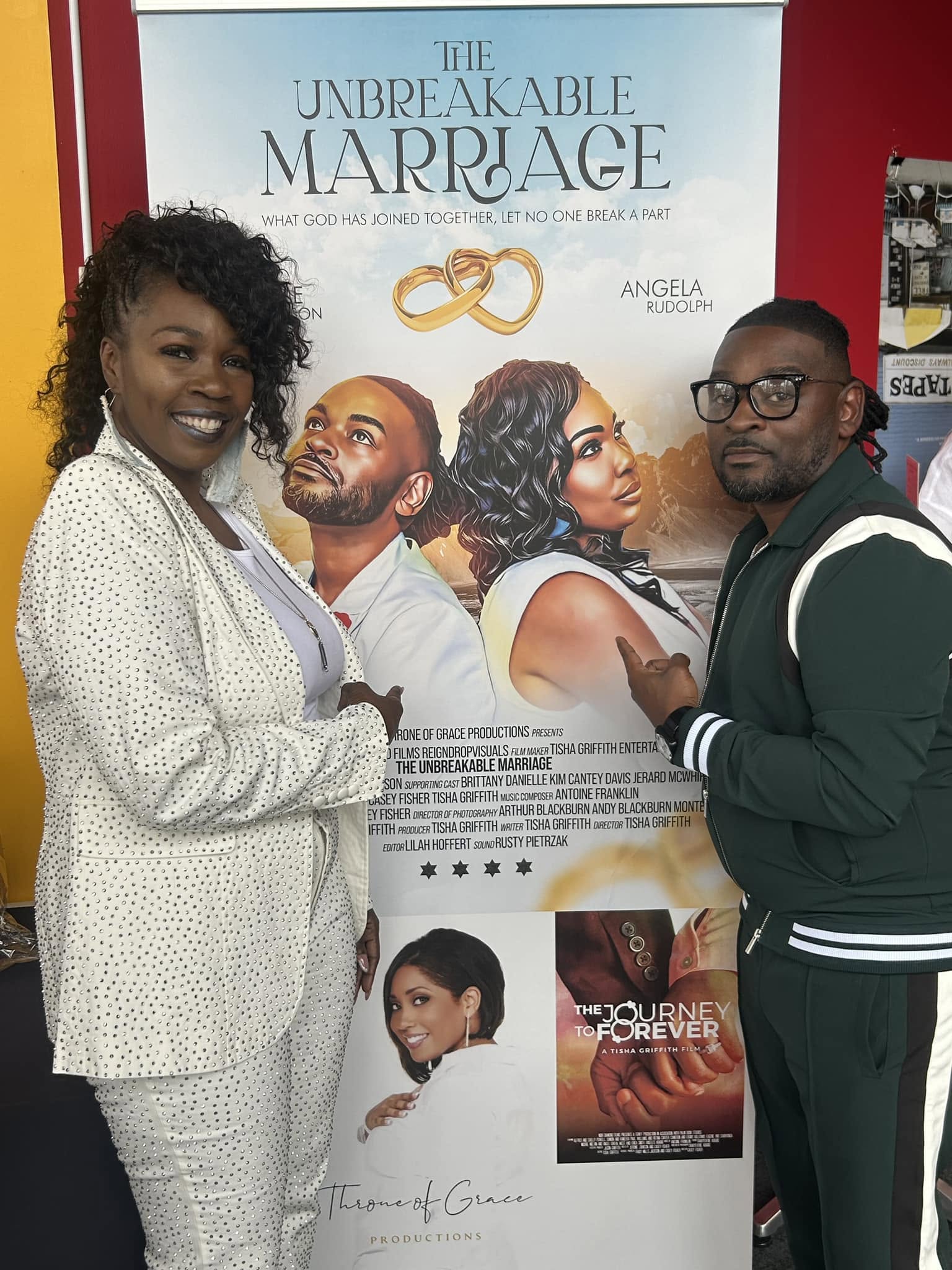 Two people stand in front of a movie poster for 'The Unbreakable Marriage,' smiling and posing for the photo.