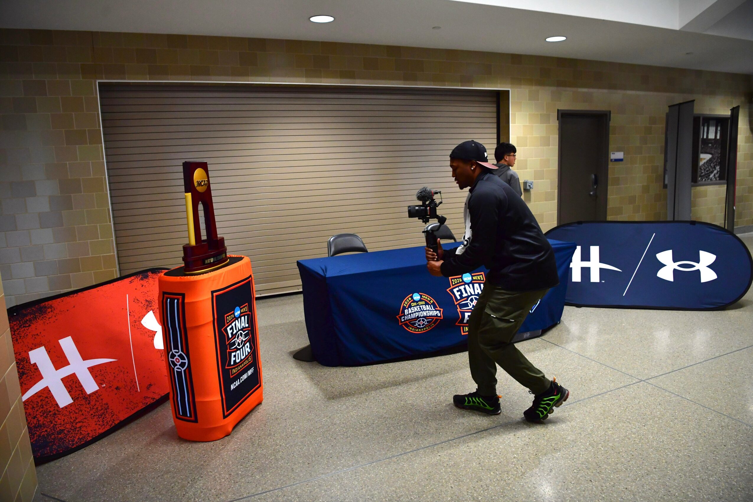 Person setting up a table with sports banners and a football-themed display in an indoor hallway.