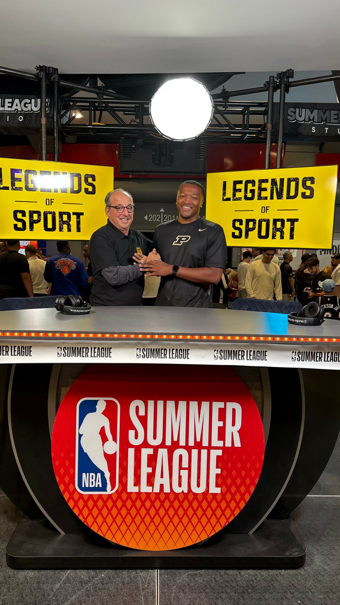 Two men shaking hands at NBA Summer League event, with banners reading 'Legends of Sport' and a large NBA Summer League logo.