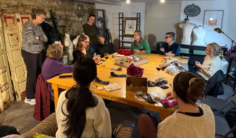 Group of people gathered around a large table in a room with stone walls and artwork, engaging in a discussion or activity.