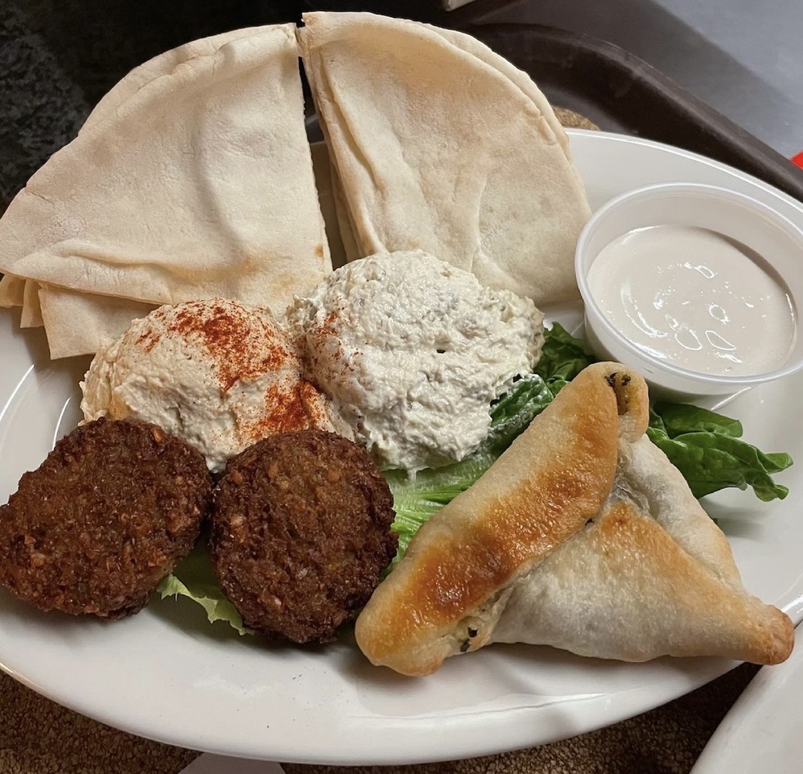 Plate with pita bread, two falafel balls, two stuffed grape leaves, two dips, and greens.