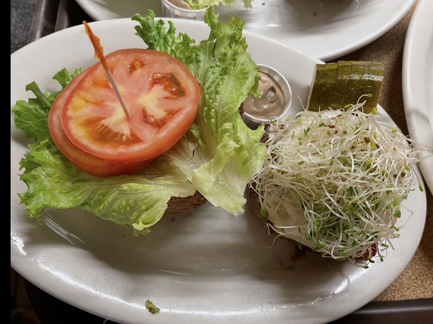 Tomato slice on lettuce with sprouts on a white plate.