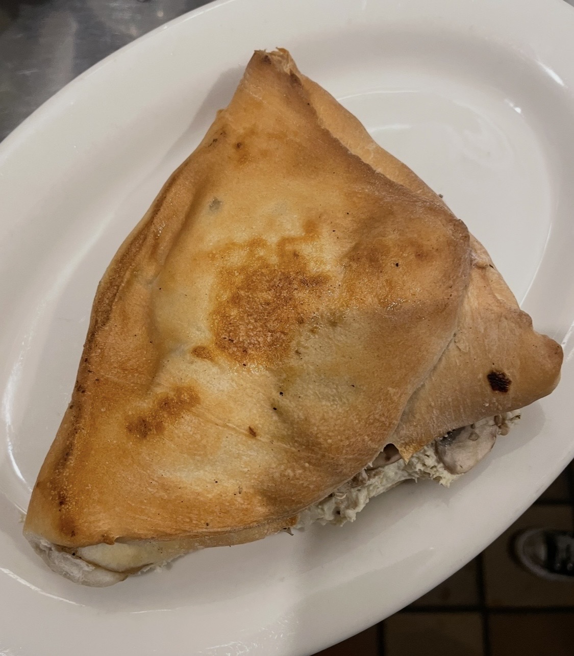 Triangular fried pastry on a white plate, partially opened revealing filling inside.