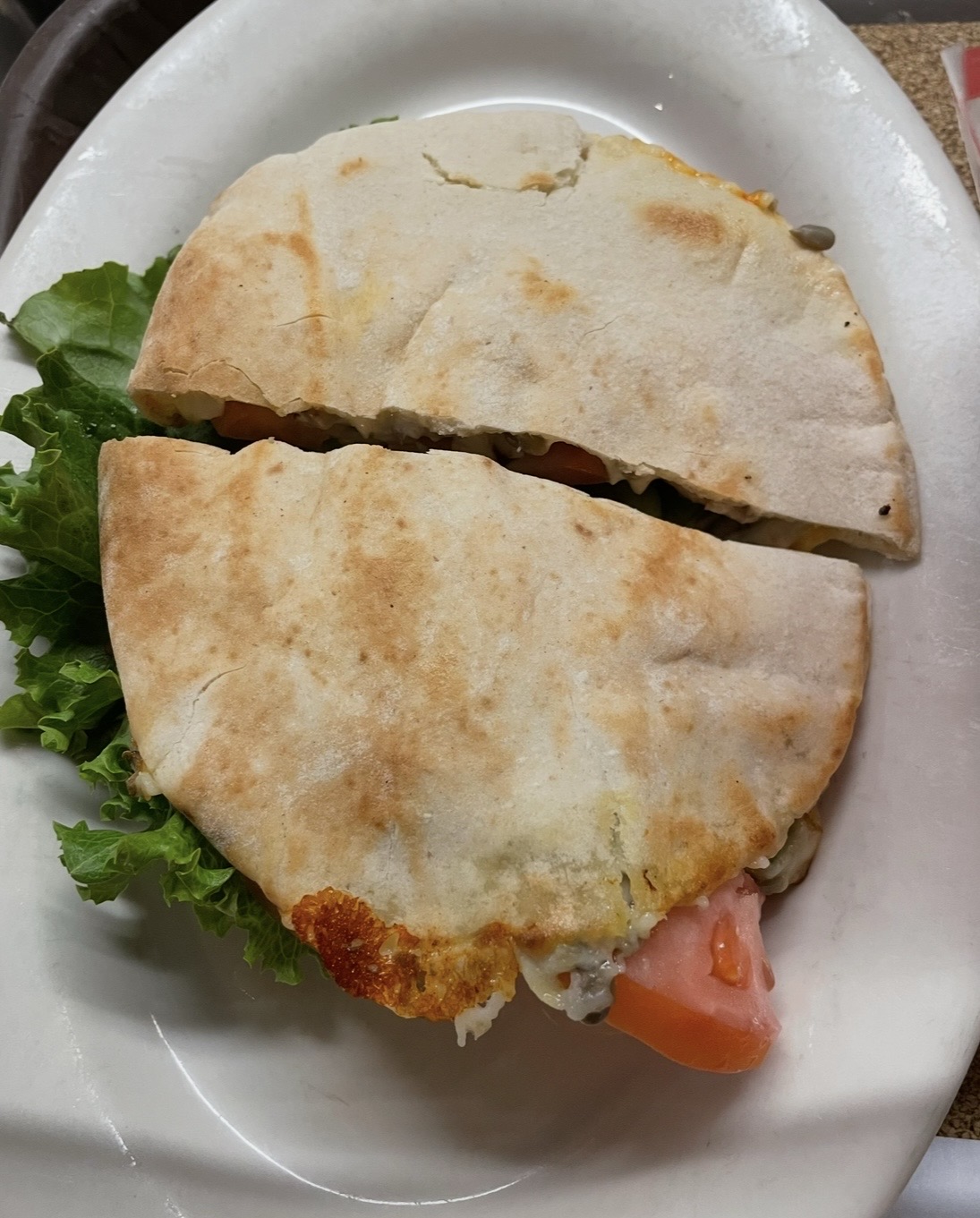 Half of a quesadilla with melted cheese and a side of leafy greens on a white plate.