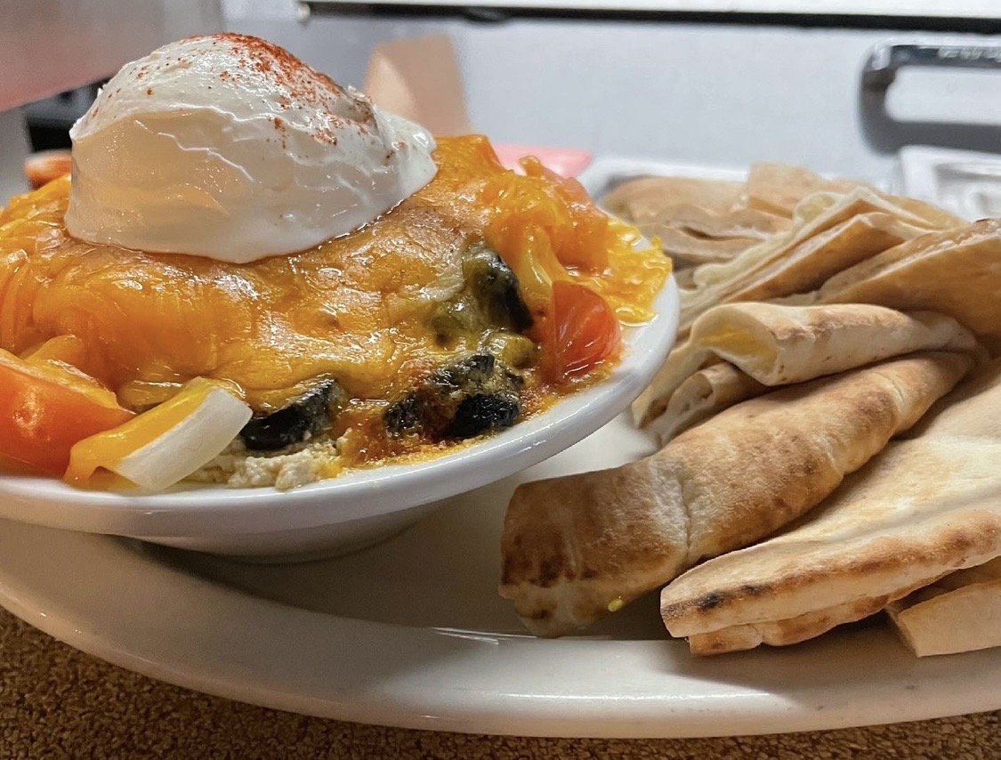 Baked dish with cheese, vegetables, and a dollop of sour cream, served with flatbread on a white plate.