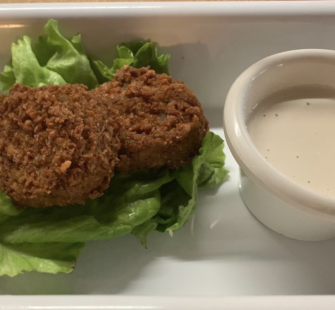 Two fried chicken pieces on lettuce with a side of white dipping sauce in a small bowl.