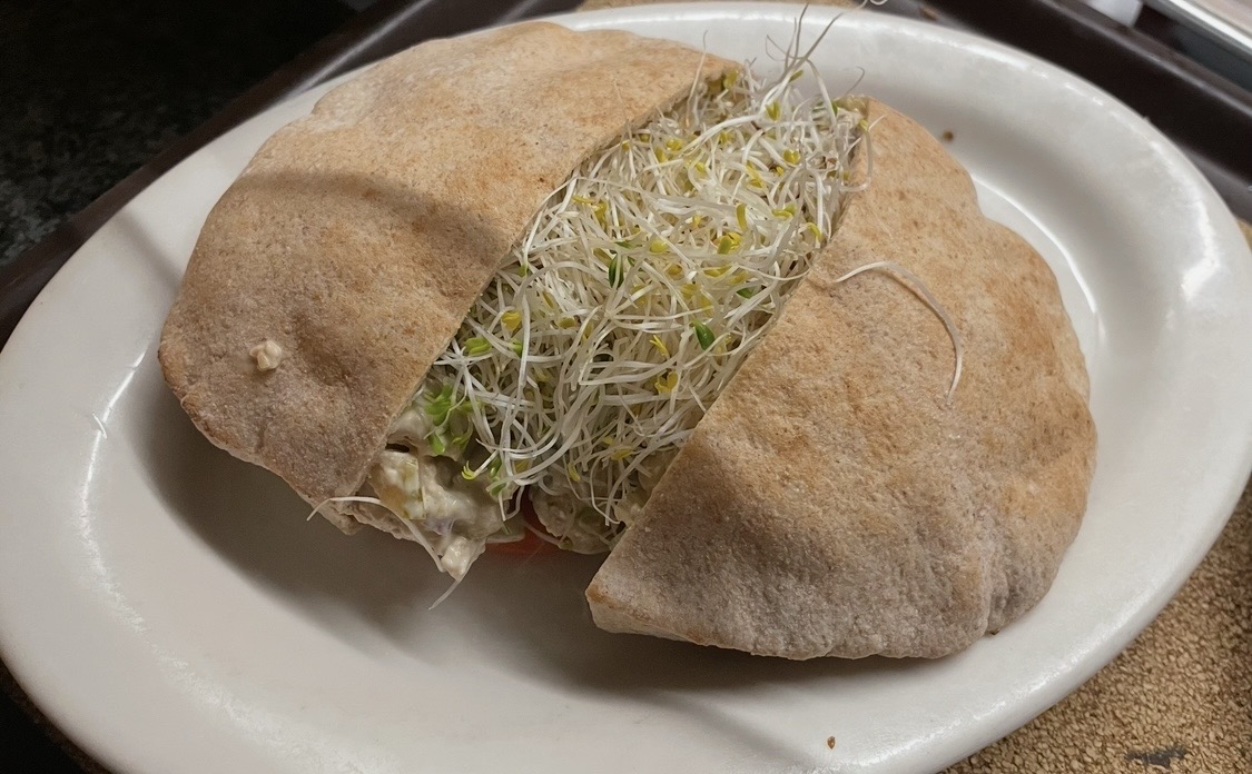 Two pita bread halves filled with sprouts and vegetables on a white plate.