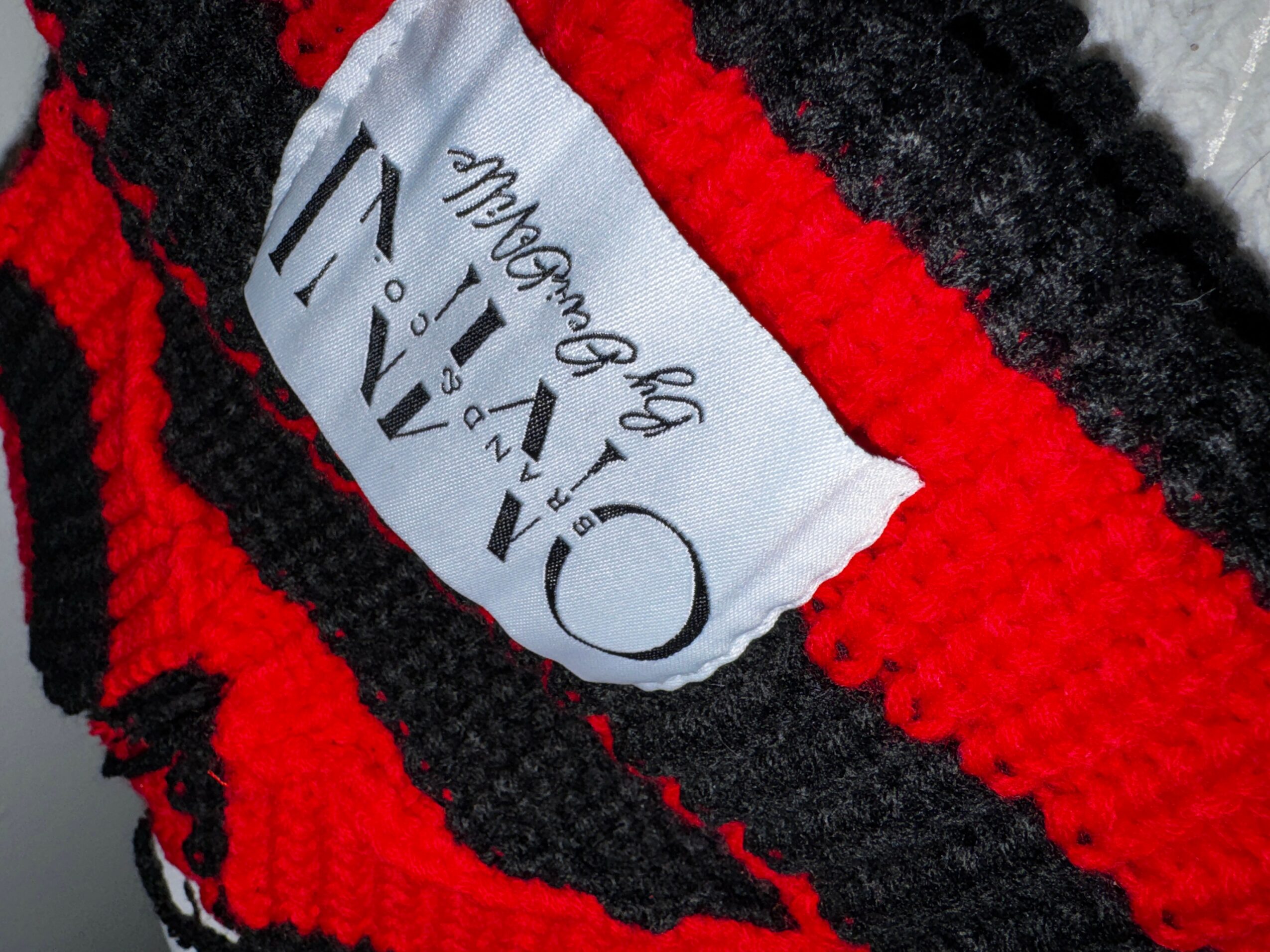 Close-up of a fabric label with black and red textured material, showing the brand name and size.