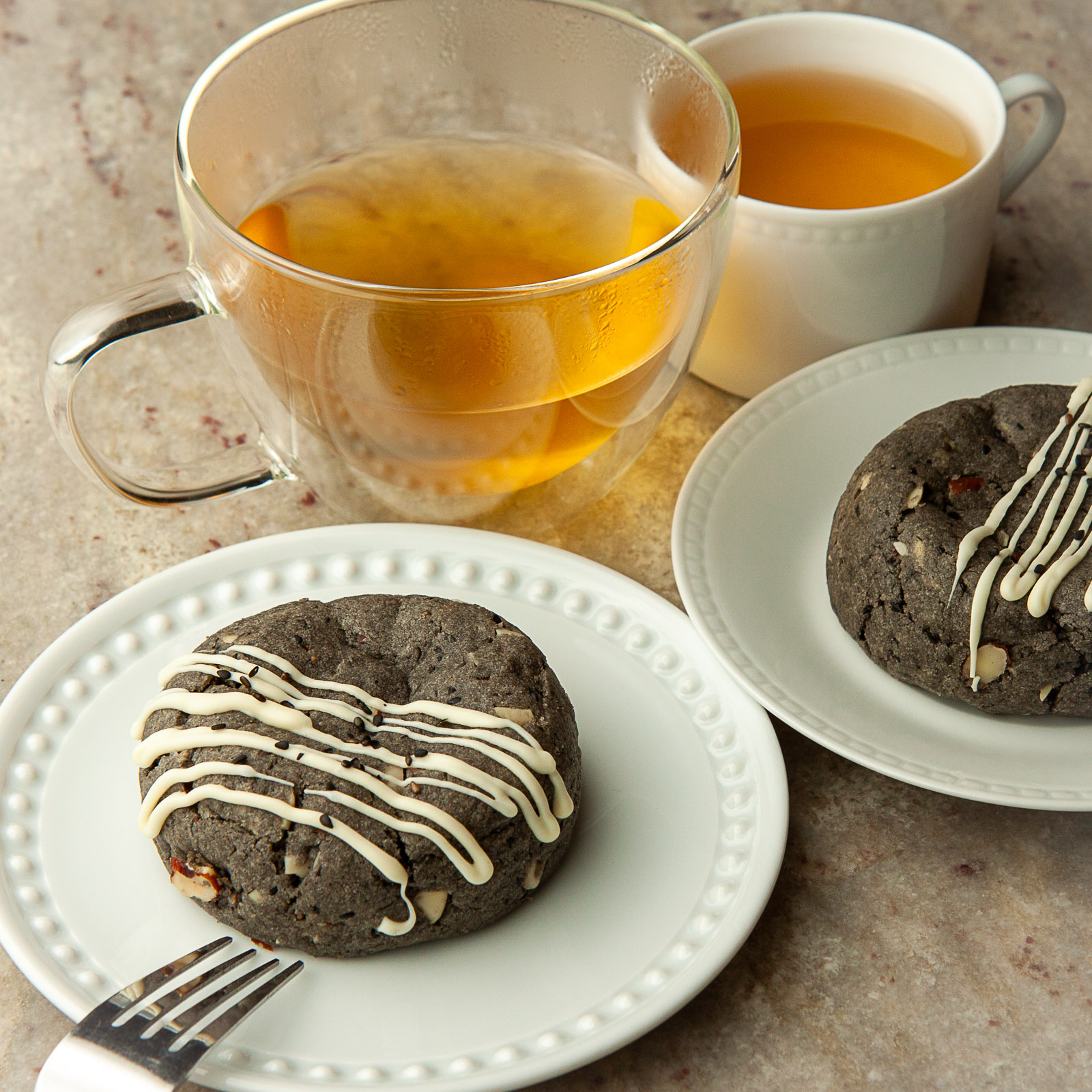 Two plates with cookies, two cups of tea, and a glass of tea on a table.