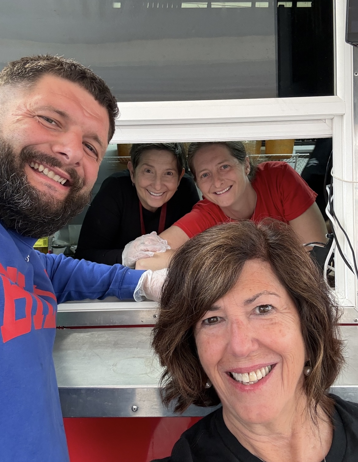 Four people smiling, two women and one man in front, and one woman behind a window, all appear happy.