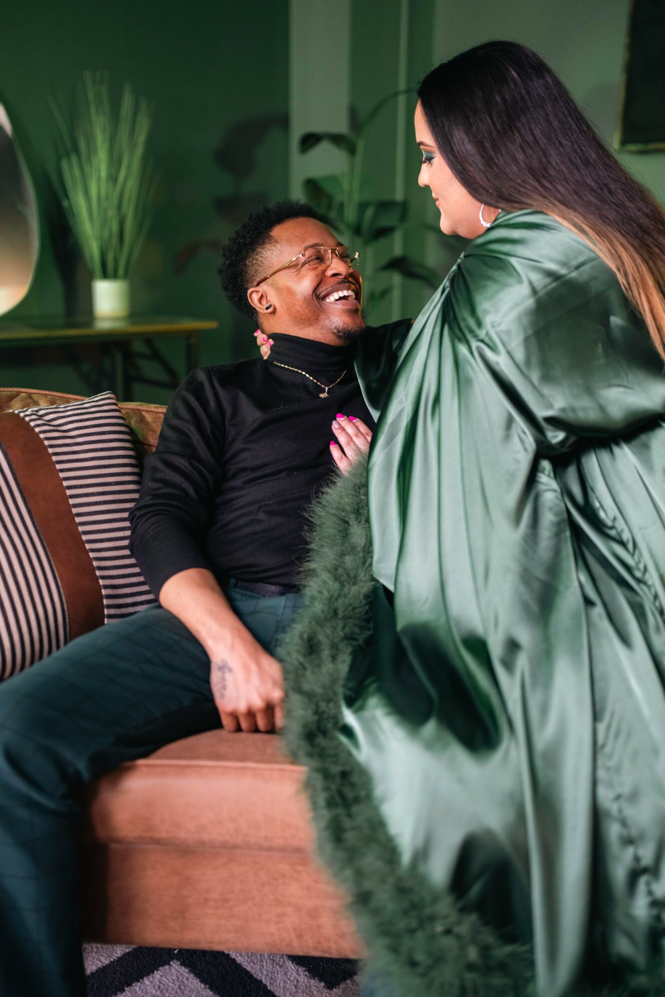 Two women smiling and talking on a sofa in a room with green walls and plants.
