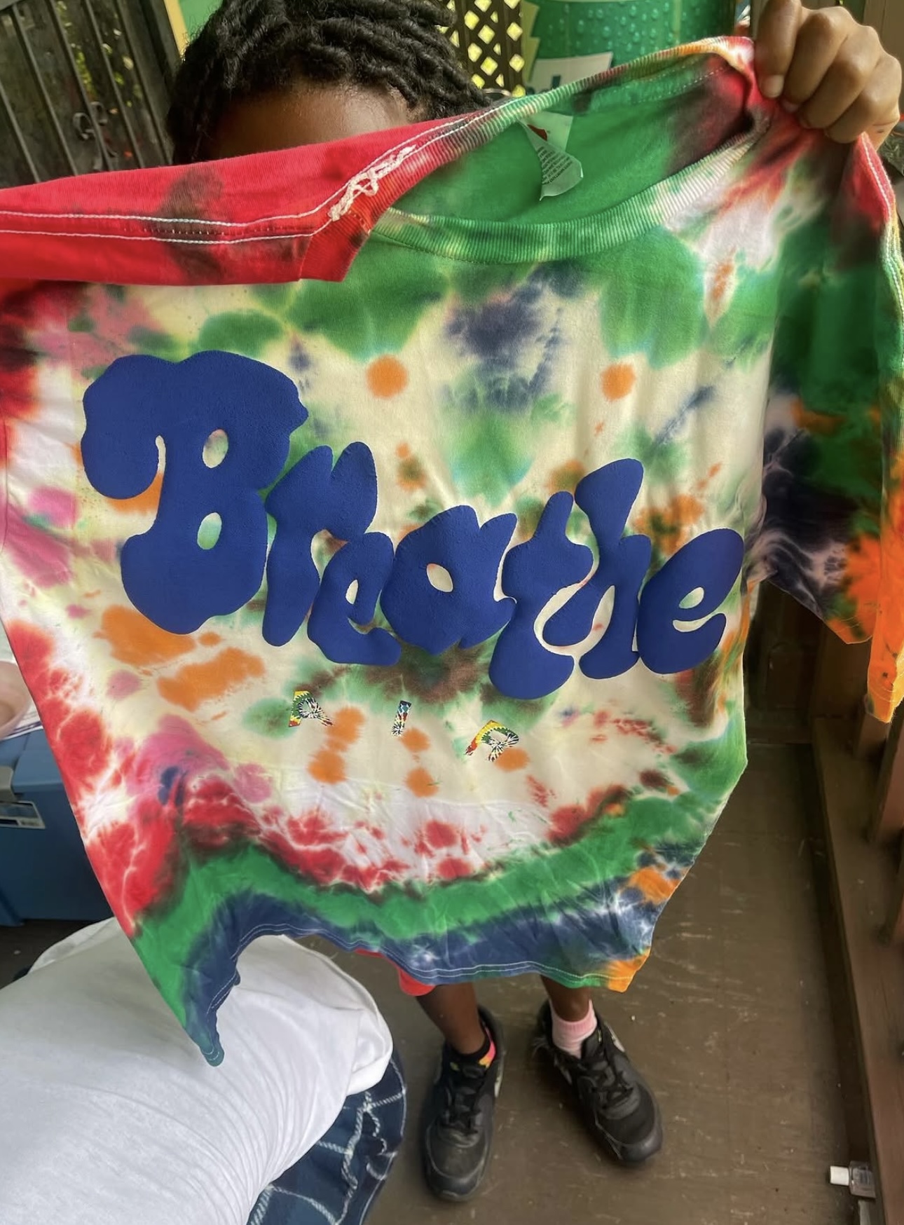 Child holding a tie-dye fabric with the word 'Breathe' in blue letters, colorful background, indoors.