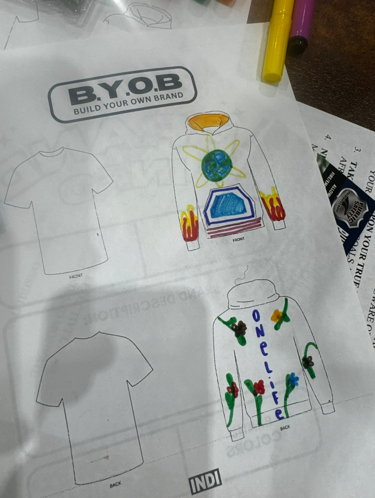 Colorful drawing of a person with a globe head, surrounded by plants and a house, on a T-shirt template, with a logo and text.