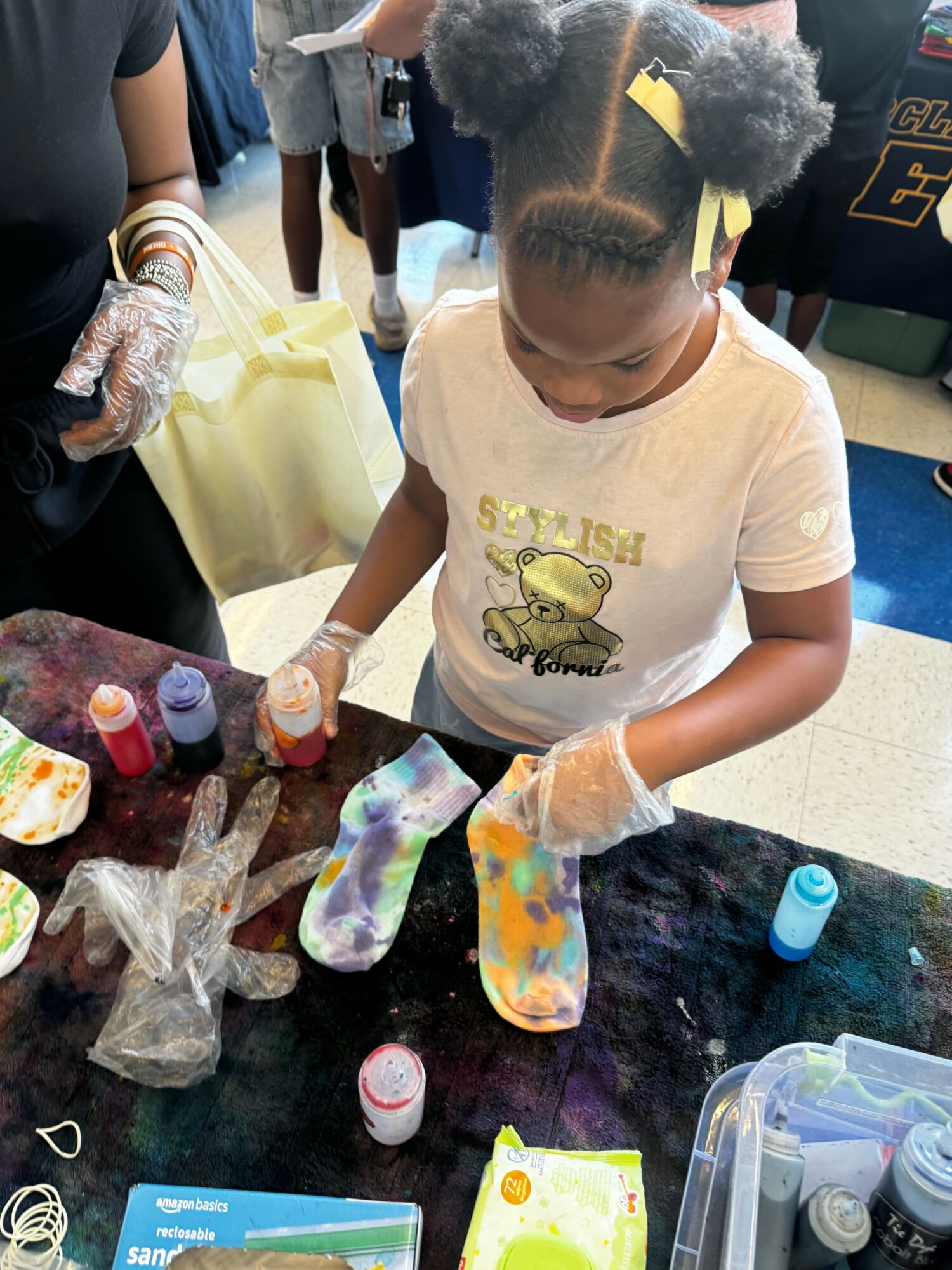 Child wearing gloves and a T-shirt with a cartoon character, working with colorful materials on a table.
