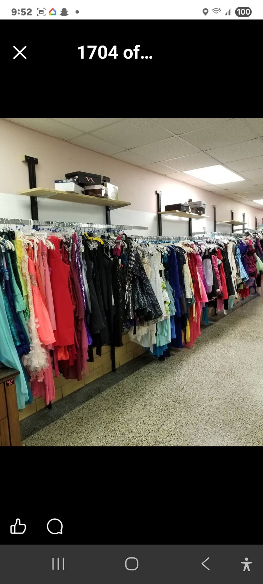 Clothing racks filled with colorful dresses and garments in a store aisle, with shelves above holding boxes and items.