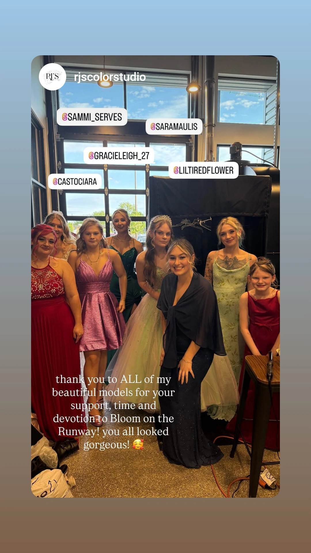 Group of women in colorful dresses posing indoors with a window and signs in the background.