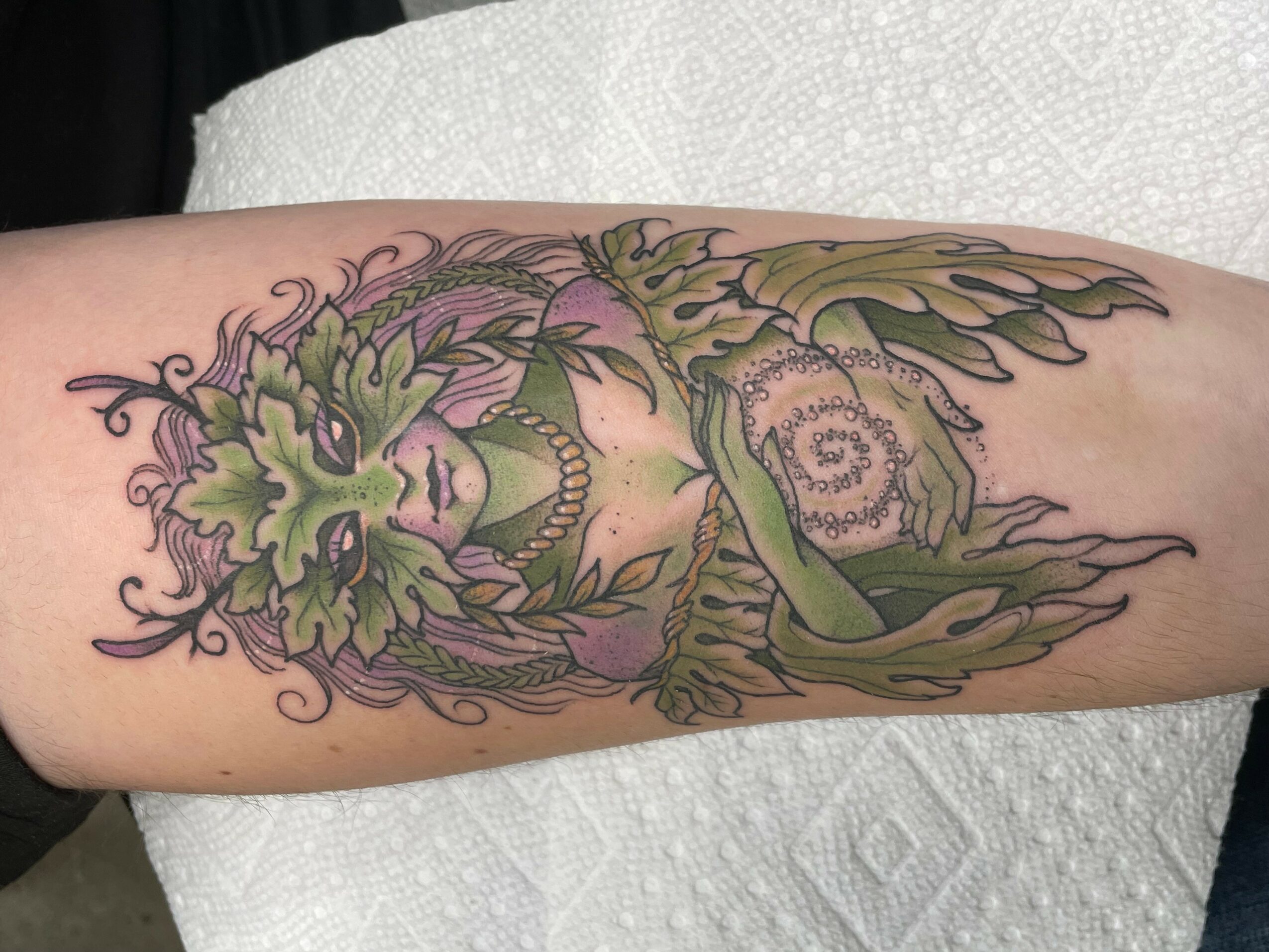 Tattoo of a green and purple floral design with intricate details on a person's arm.