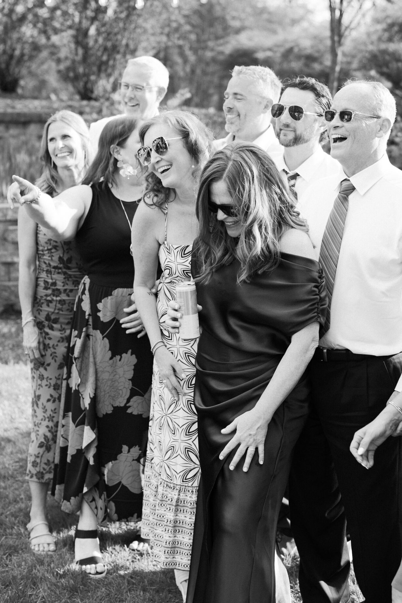 Group of people outdoors, smiling and posing for a photo, some wearing sunglasses, in black and white.