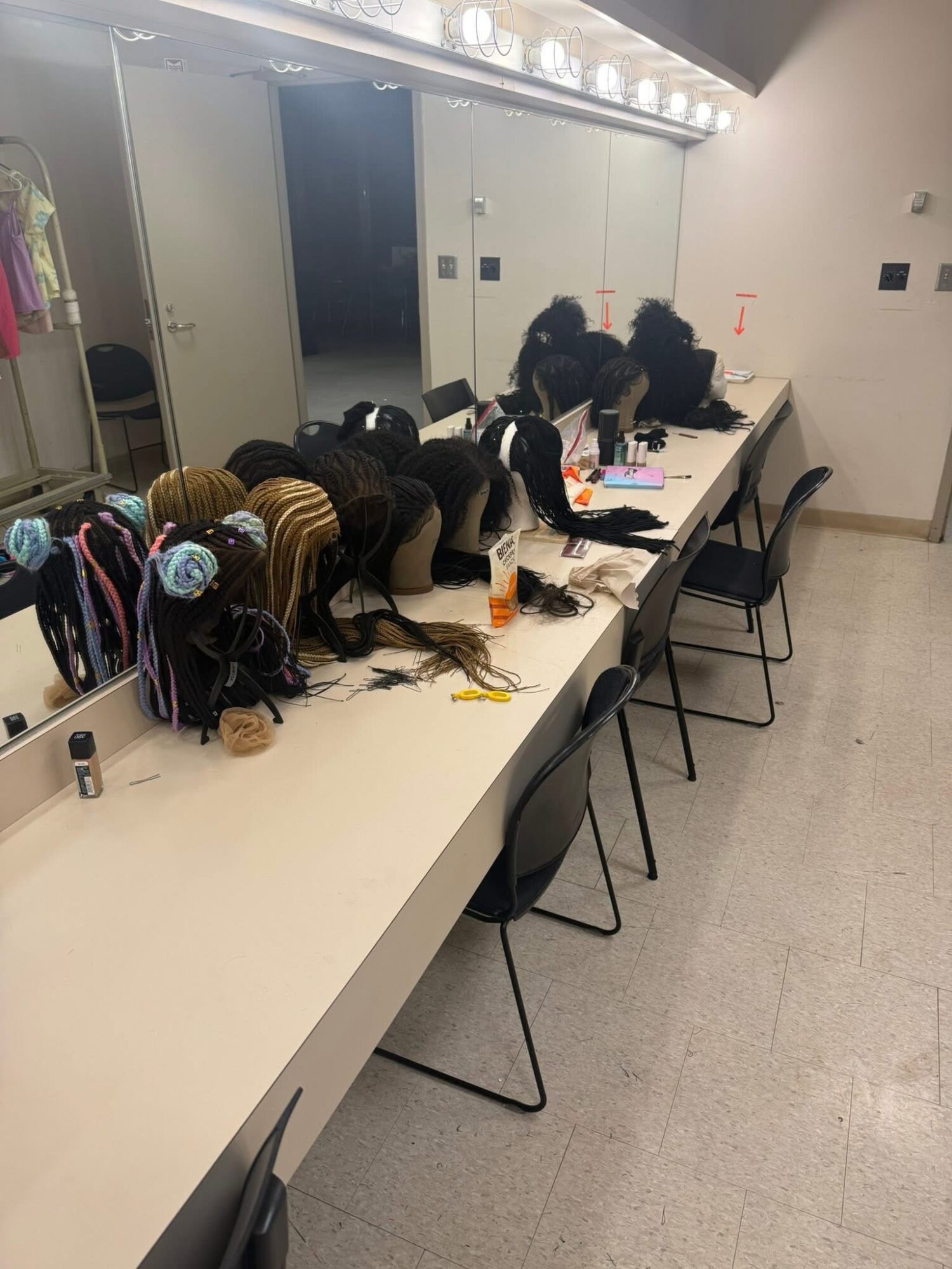 Group of people sitting at a long table, working on laptops and writing, in a room with lockers and a mirror.
