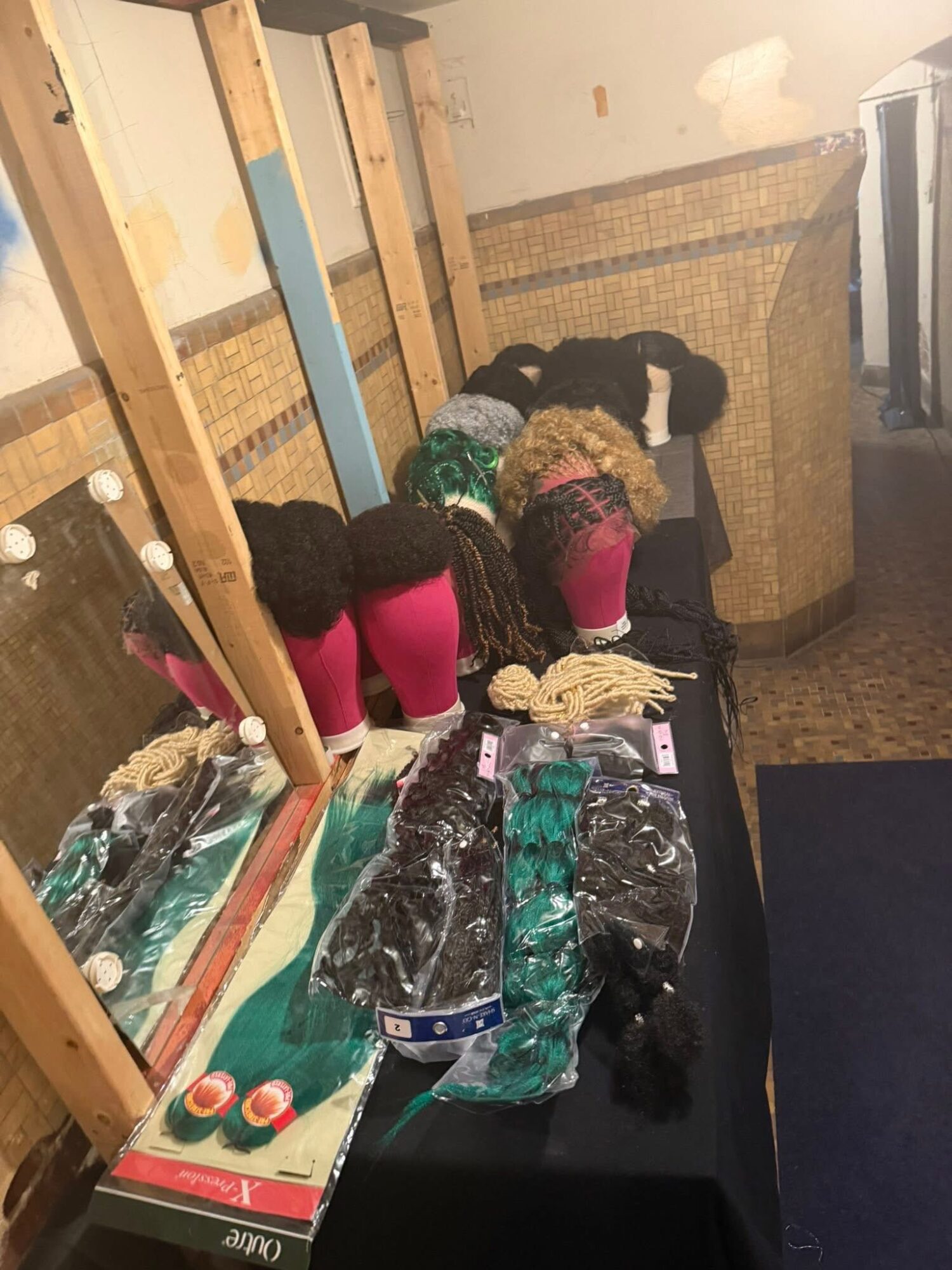 Four children with curly hair bend over a table, looking at items, in a room with wooden framing and a woven wall. Word count: 20