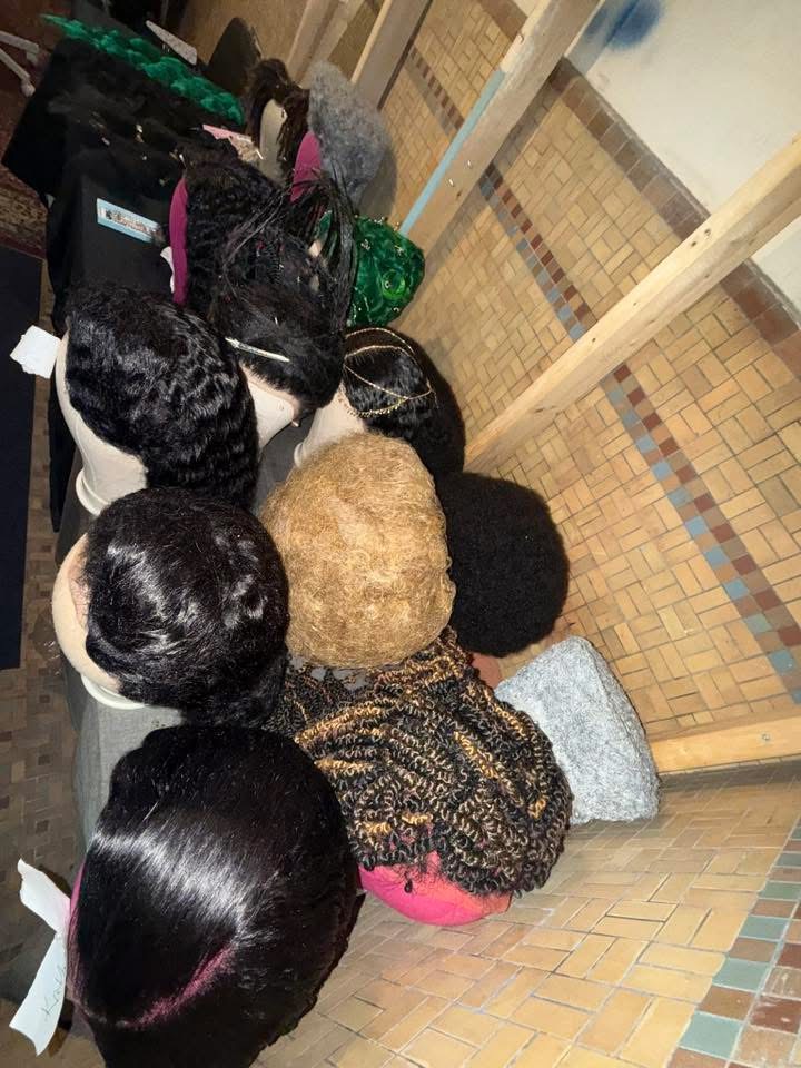 Multiple black and gray hairpieces or wigs displayed on a table, with a tiled floor and wooden railing in the background.