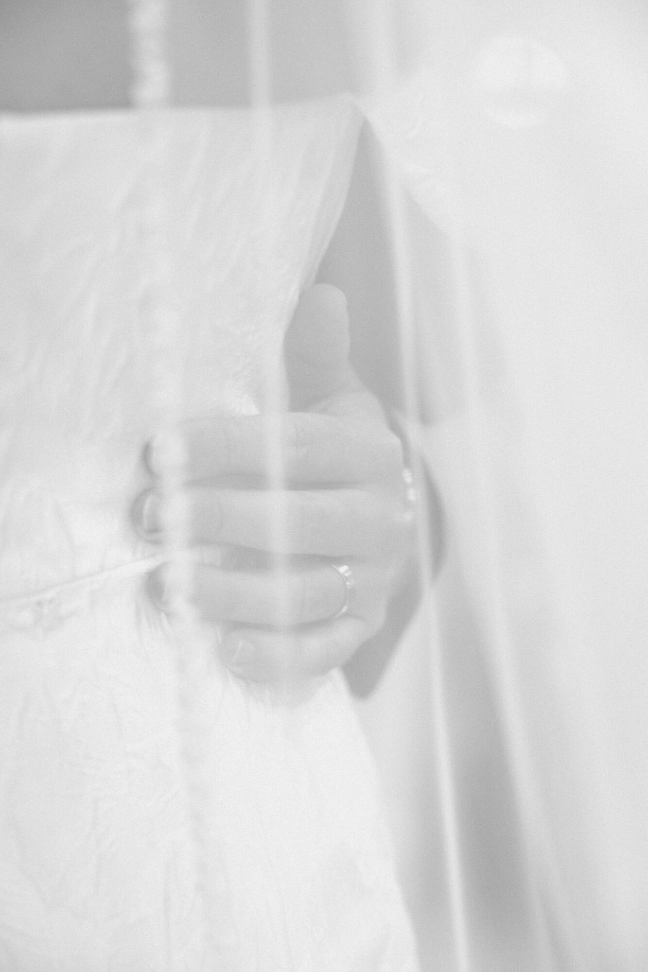 Person holding a small object, partially obscured by a sheer curtain, in a bright setting.