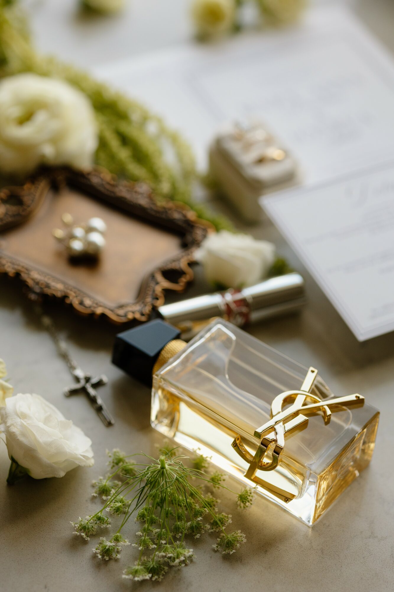 Perfume bottle, jewelry, and flowers on a surface with papers in the background.