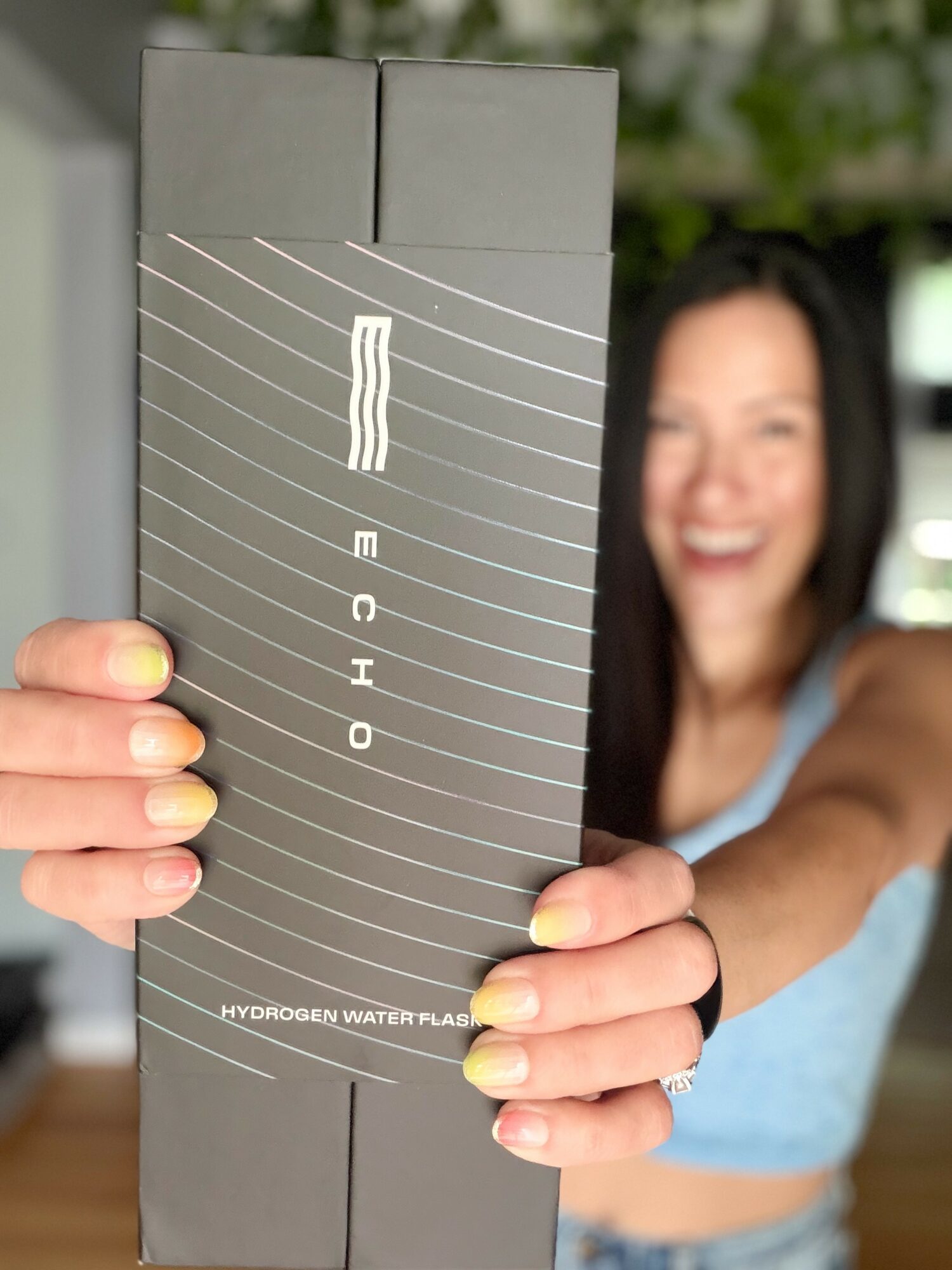 Person holding a hydrogen water flask with a blurred smiling woman in the background.