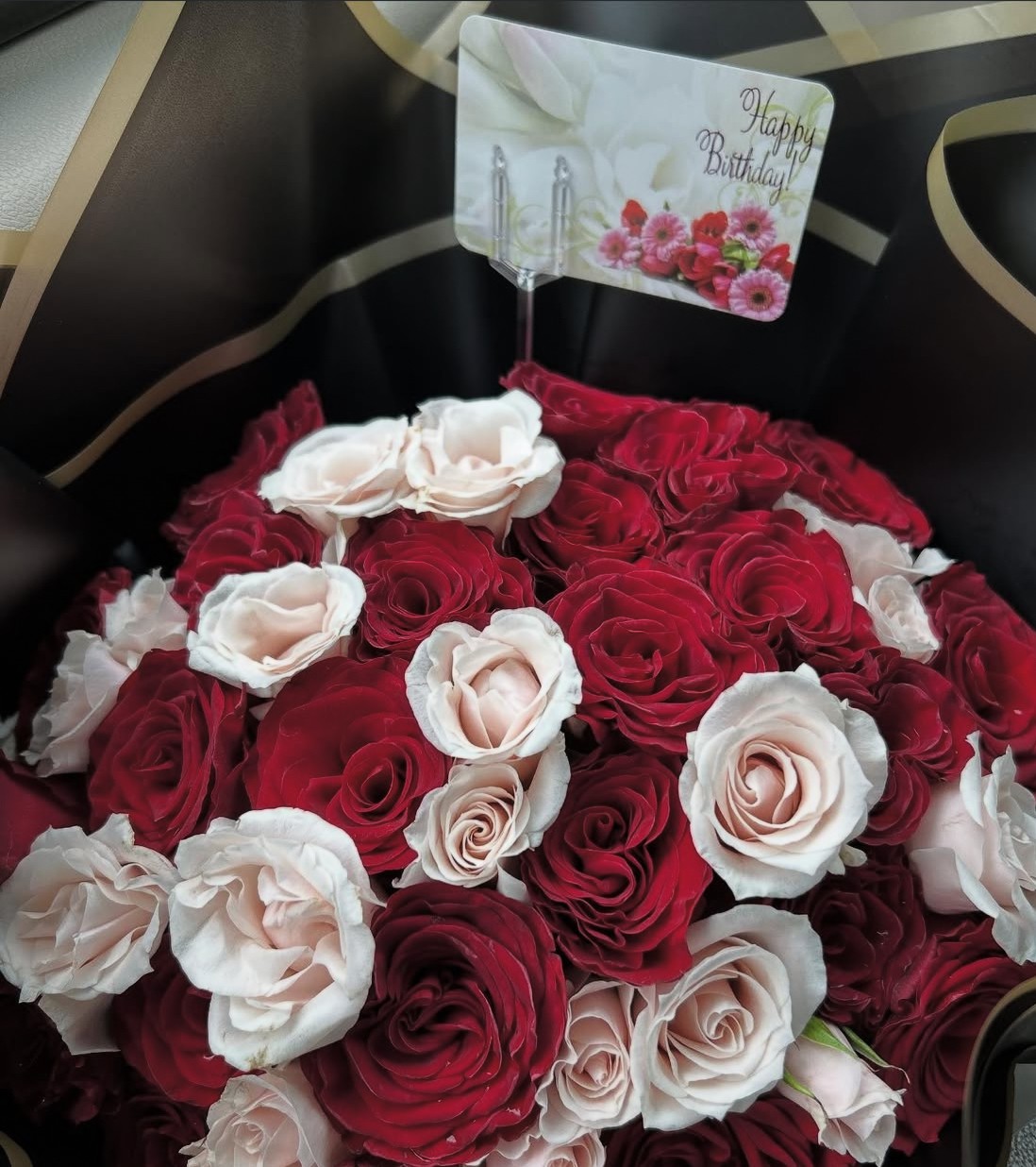 A basket filled with red and white roses, with a birthday card that says 'Happy Birthday' in the background.