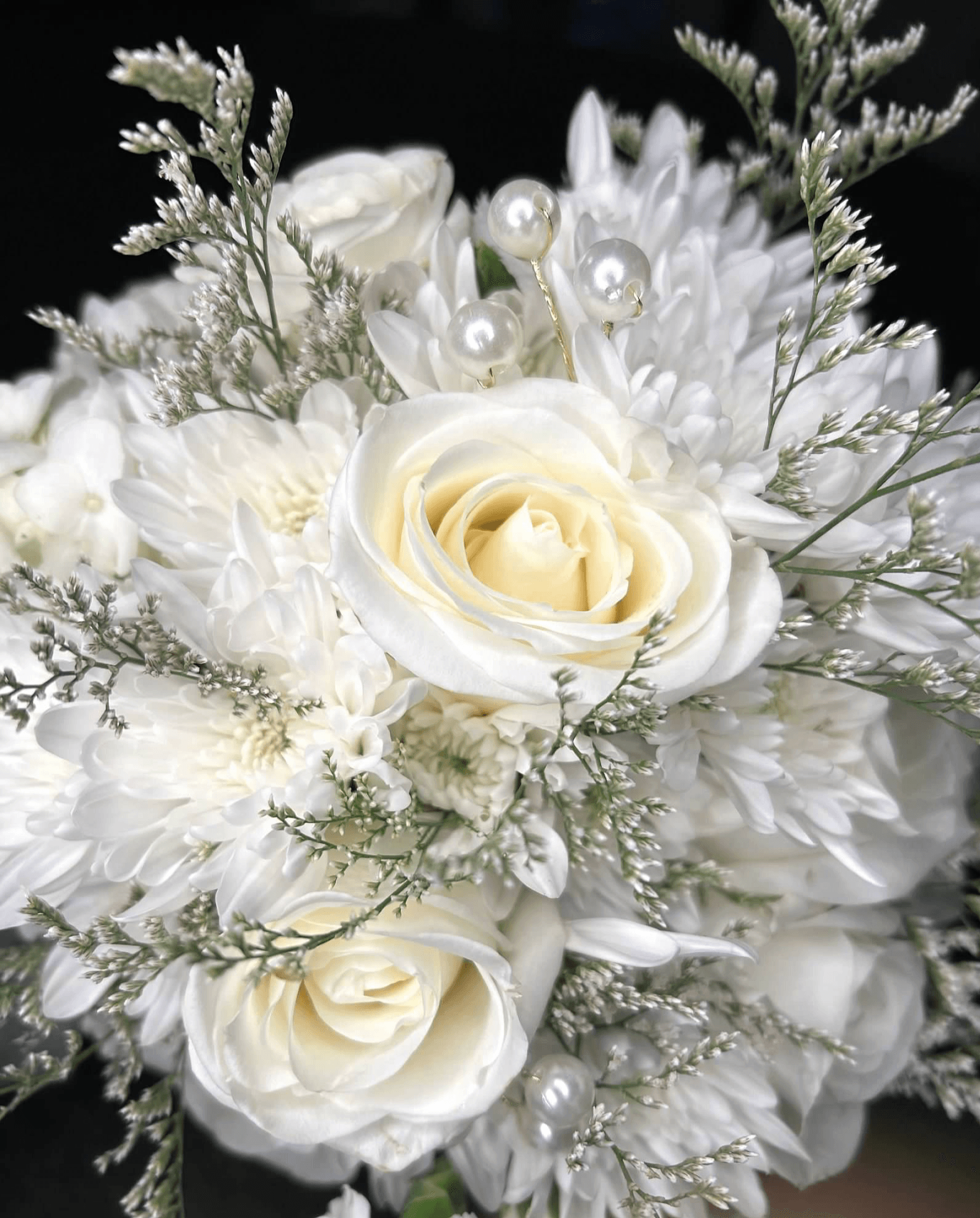 White floral bouquet with roses, pearls, and greenery, arranged against a black background.