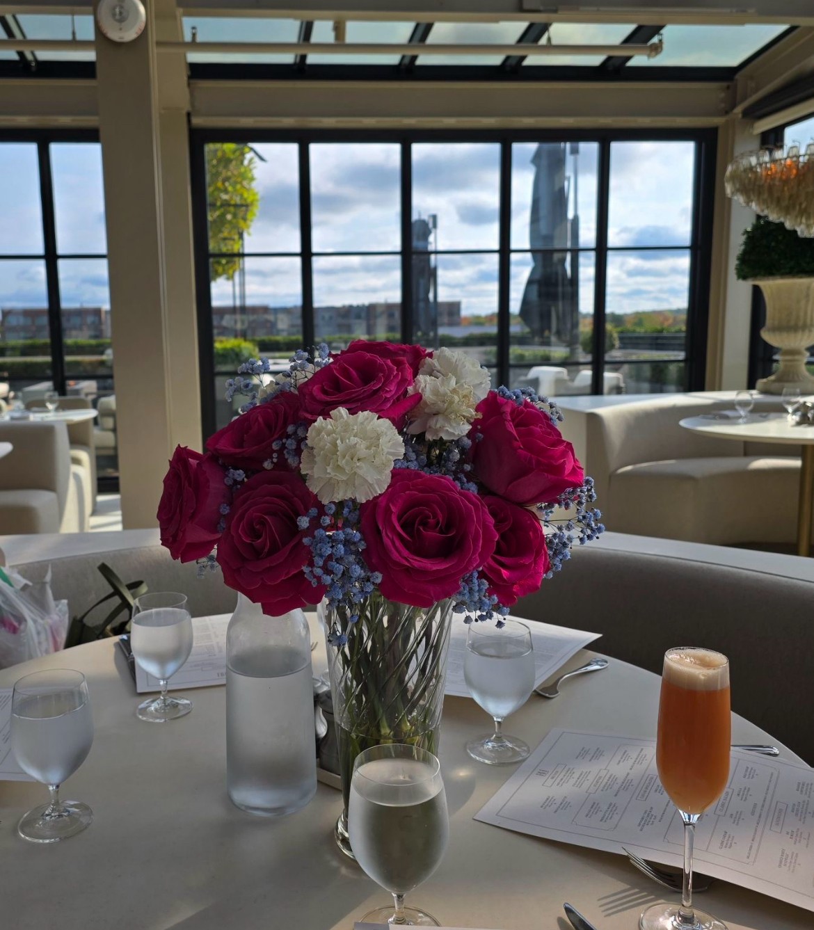 Vase with pink and white flowers on a table in a bright room with large windows and outdoor view.