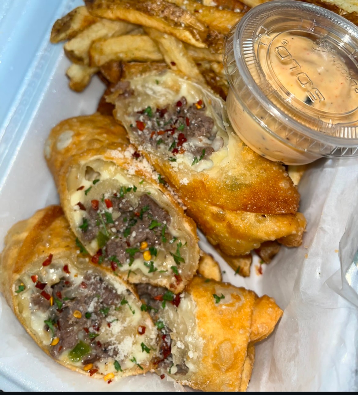 Fried egg rolls with chopped vegetables and meat filling, served with dipping sauce in a plastic container, on a tray.