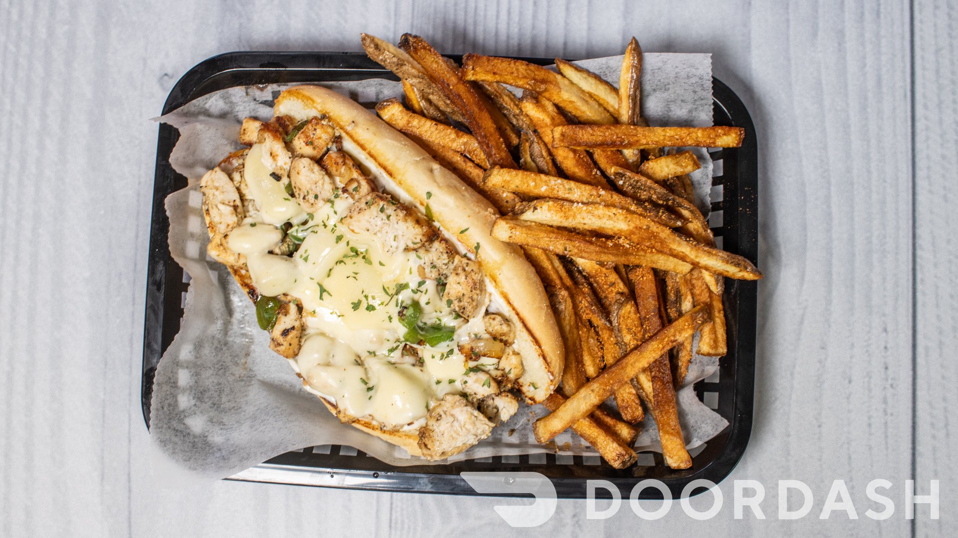 Sandwich with melted cheese and herbs, served with French fries on a black tray, lined with parchment paper.