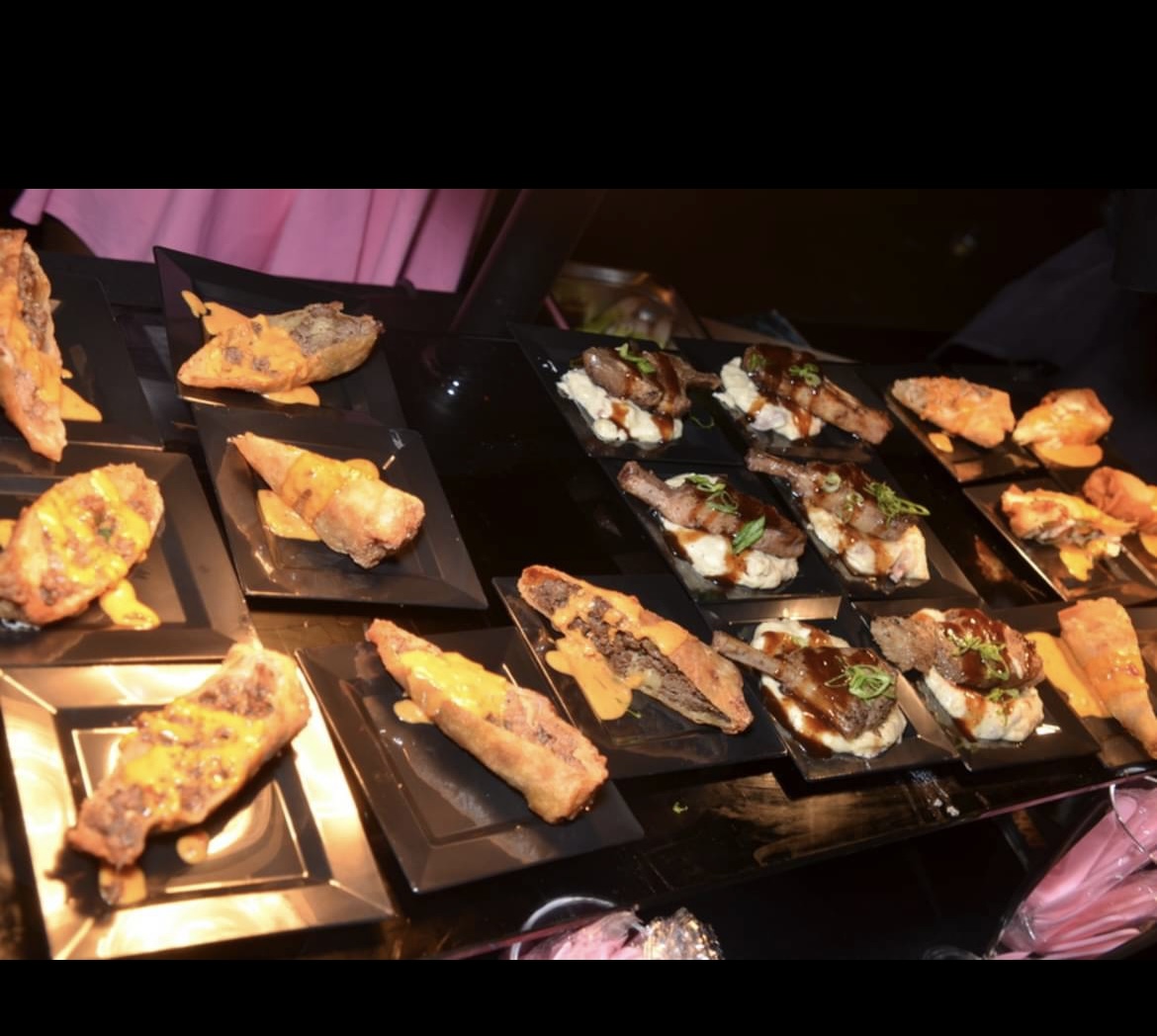 Assorted pieces of sushi and tempura on black plates arranged on a table, with some pink fabric in the background.