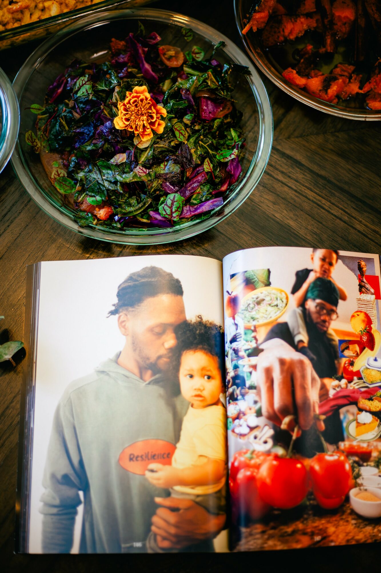 Open magazine showing a man holding a child, with colorful food and a salad bowl on a wooden table nearby.