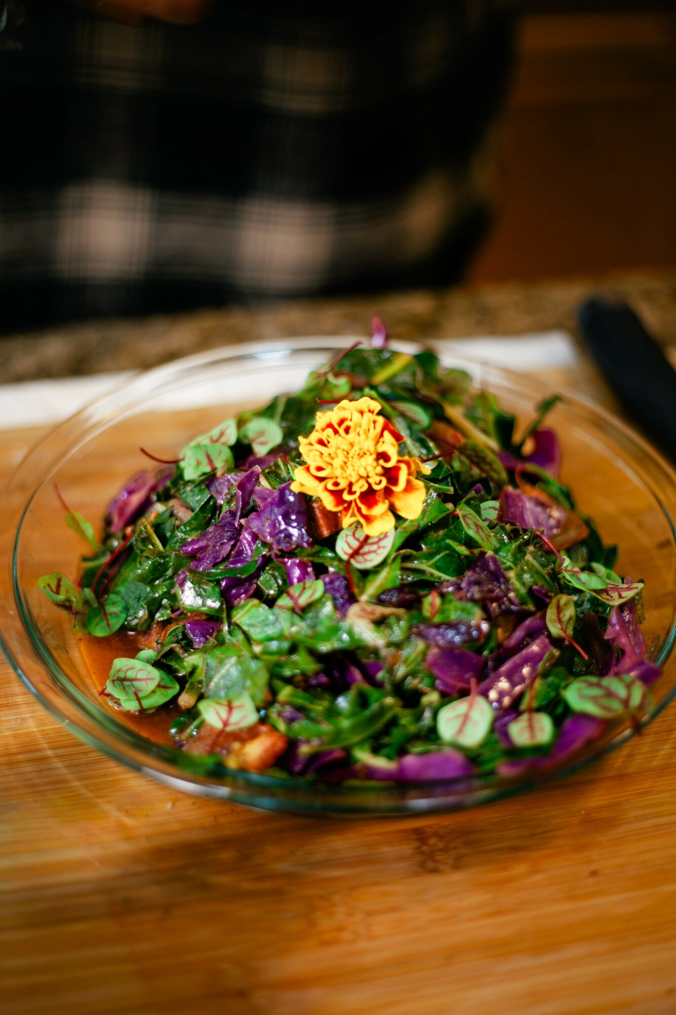 Colorful salad with purple, green, and yellow ingredients on a glass plate, placed on a wooden surface.