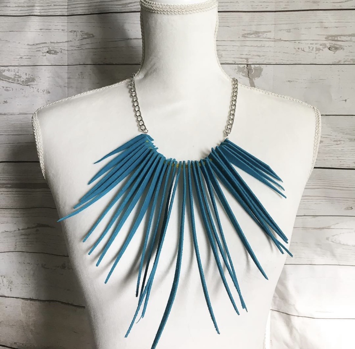 Necklace with blue elongated spikes on a white mannequin bust, against a wooden background.