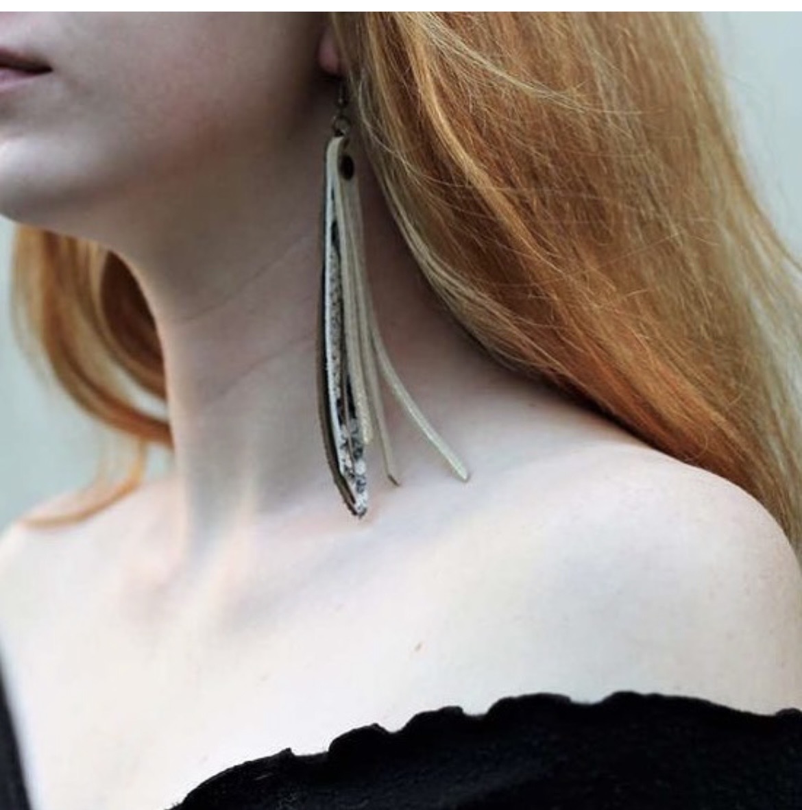 Close-up of a woman with red hair wearing a large, dangling earring and a black off-shoulder top.
