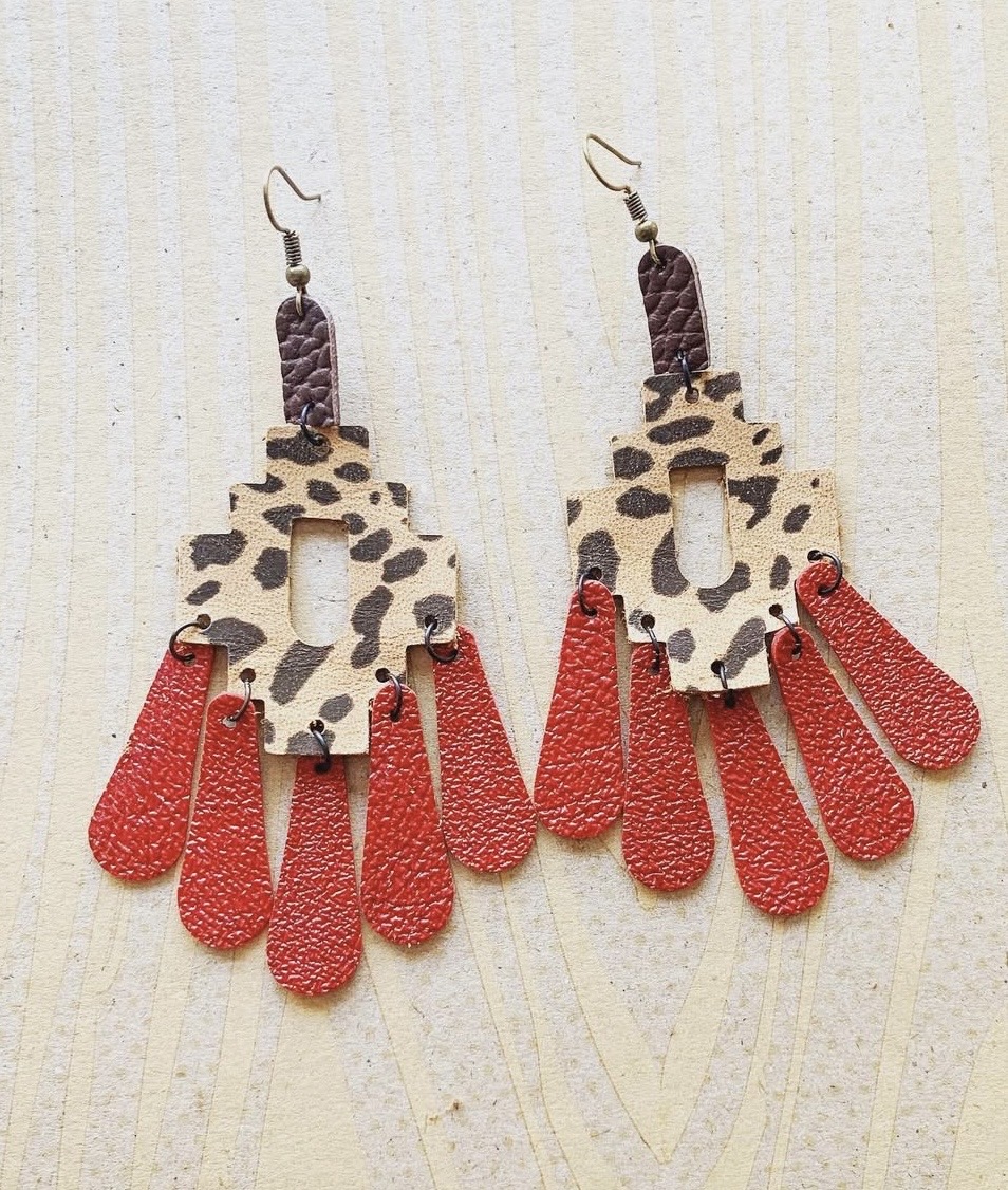 Pair of earrings with leopard print and red teardrop-shaped elements hanging from a beige background.