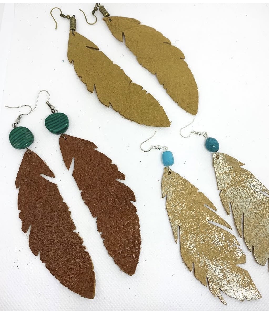 Three pairs of feather-shaped earrings in gold, brown, and gold with glitter, each with different colored hooks or studs, on a white background.