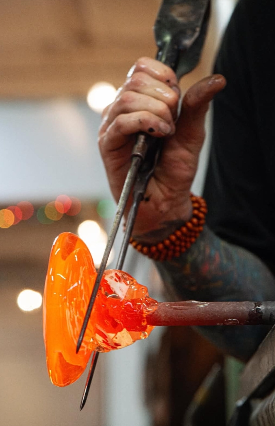 Glassblower shapes molten glass using tools, with a focus on the glowing orange glass piece.