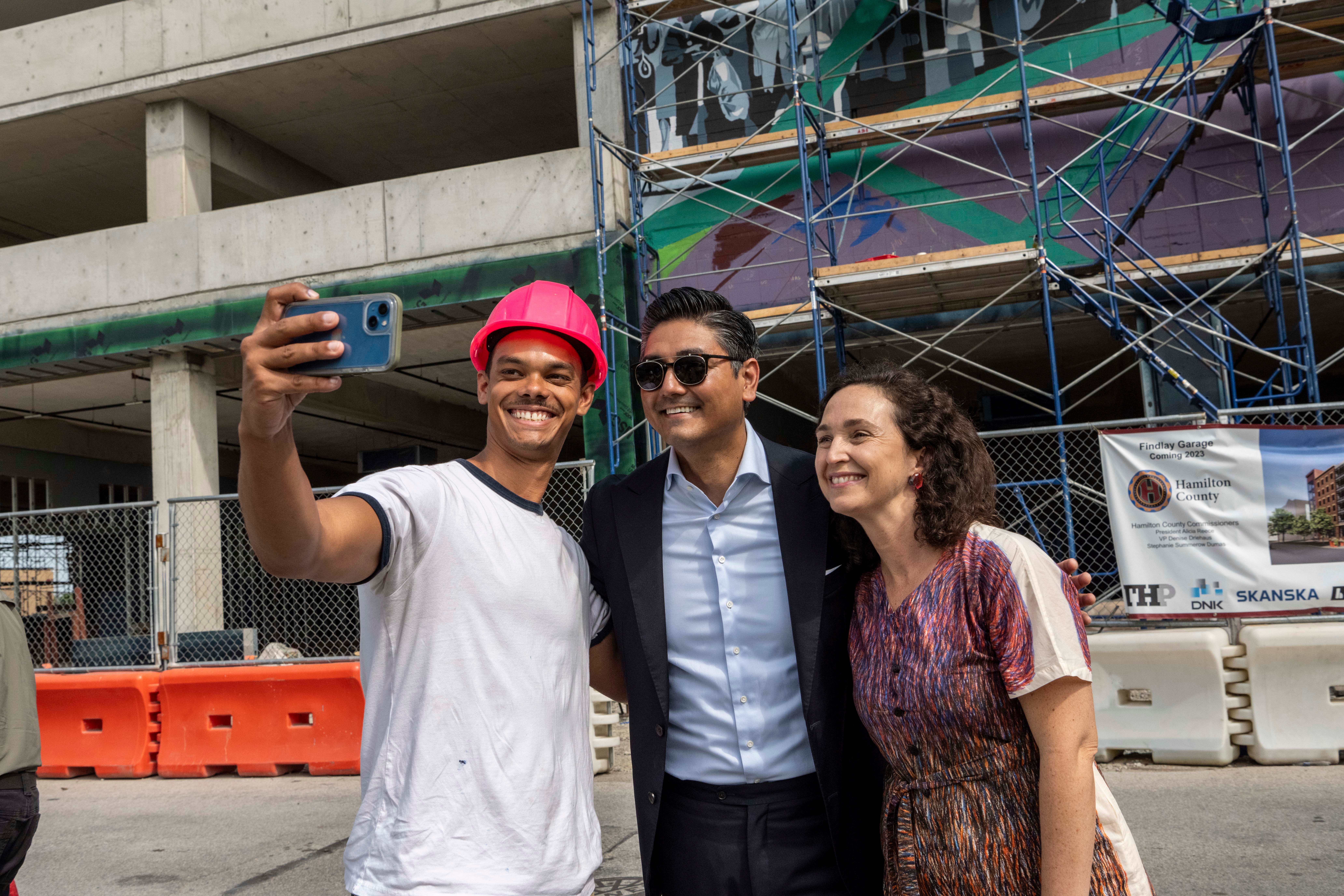 Three people taking a selfie outdoors, smiling, with construction and scaffolding in the background.