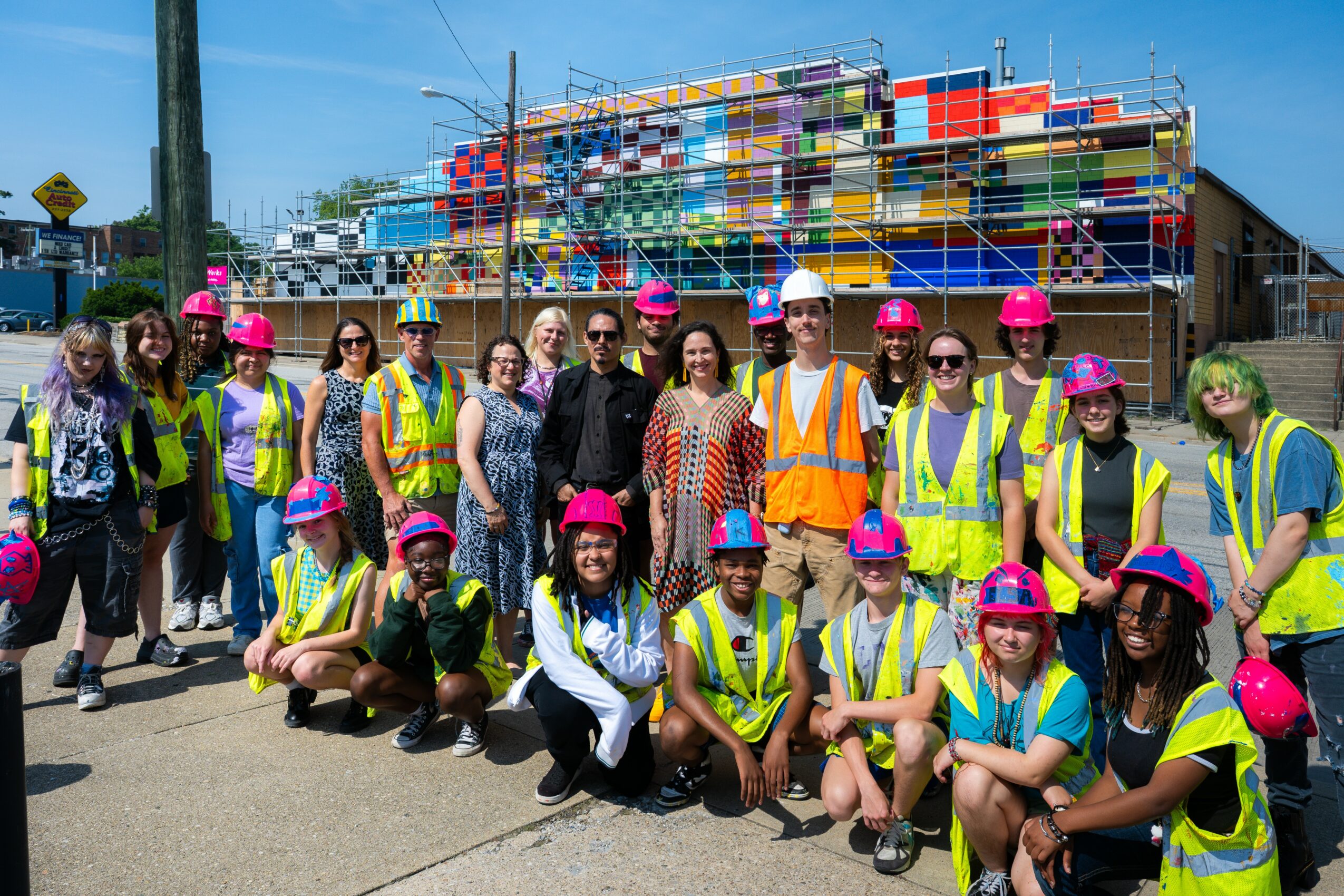 Group of people wearing safety vests and helmets in front of a colorful building under construction.