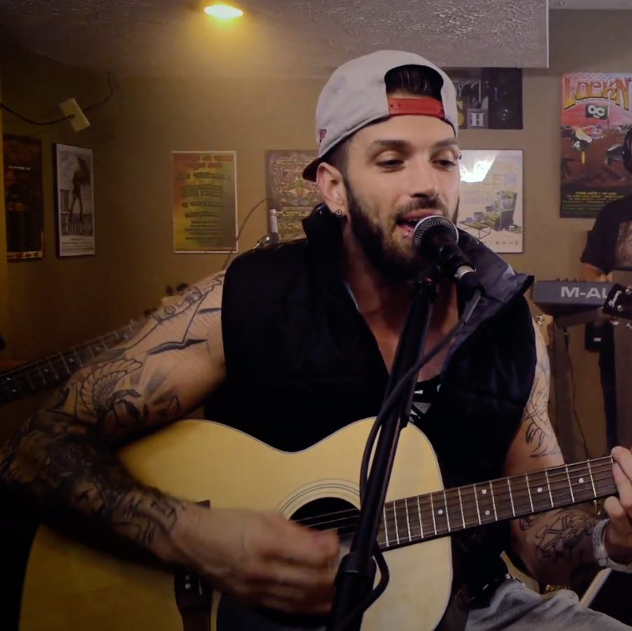 Man playing guitar and singing into microphone in a room with posters on the wall.