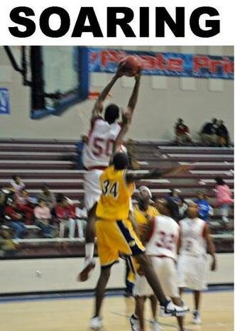 Basketball player in white jumps to block yellow player's shot during game, with spectators in background.