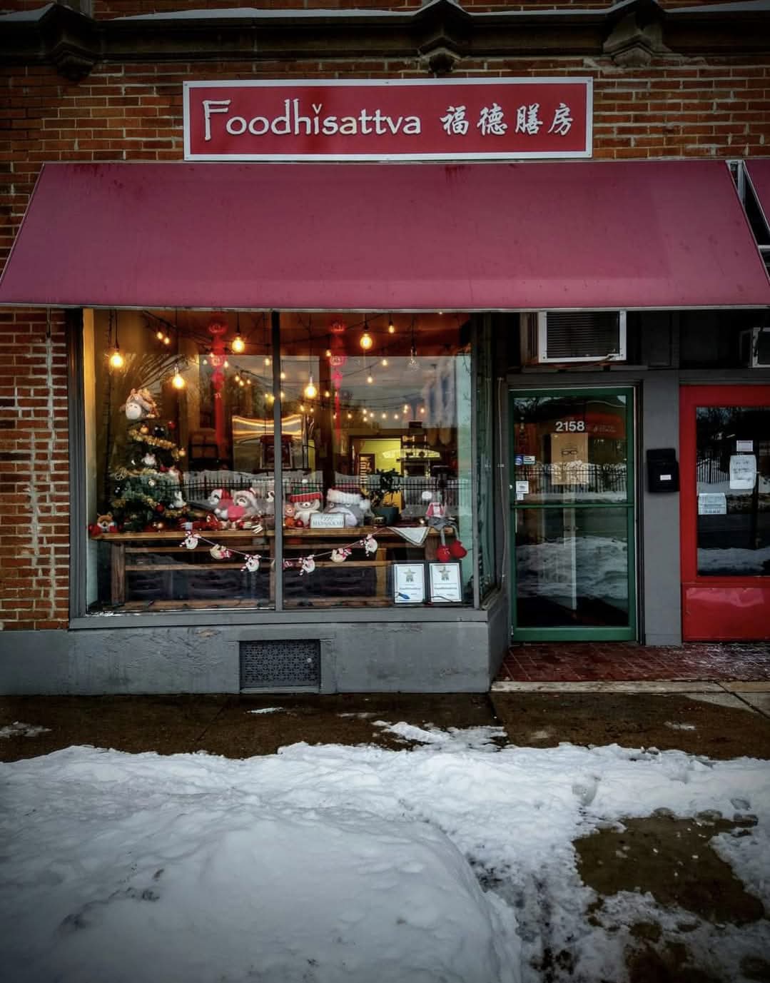 Storefront with a red awning, large glass window displaying baked goods, and a sign reading 'Foodhisattva' in English and Chinese.