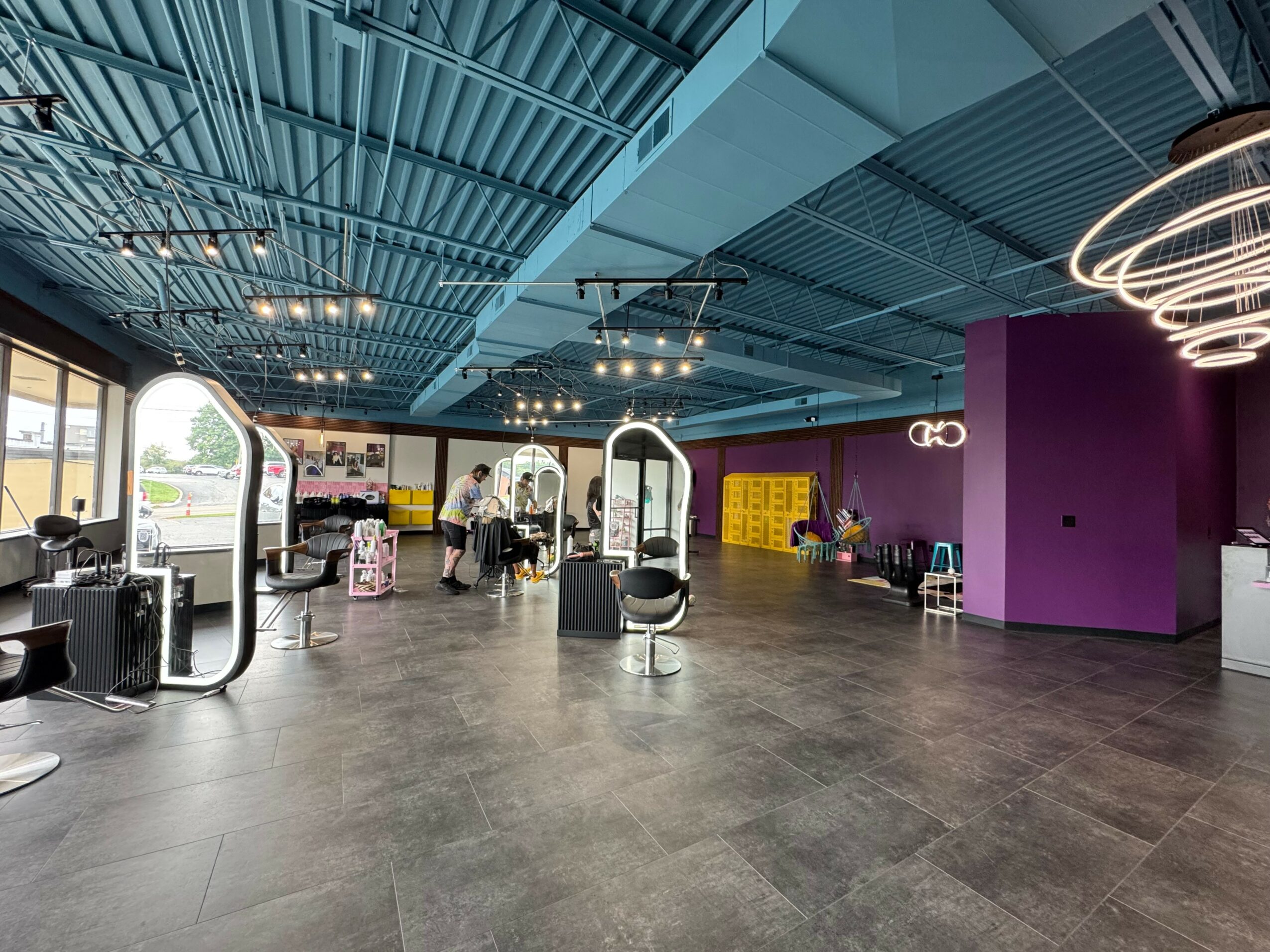 Interior of a modern space with high ceiling, purple wall, seating, and people near windows.