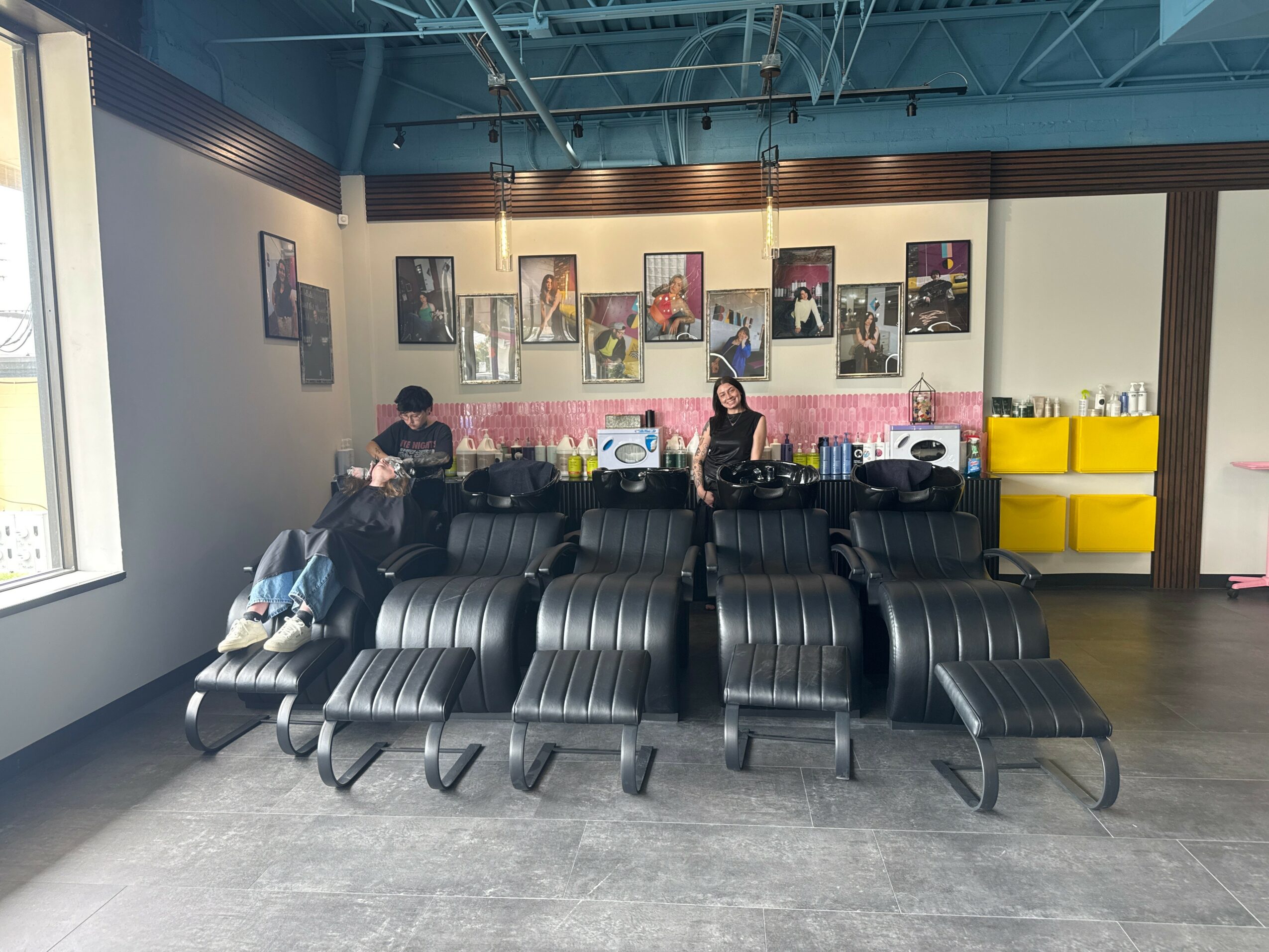 Waiting area with black chairs, a woman, a child, and a wall with framed pictures, a window, and yellow storage units.