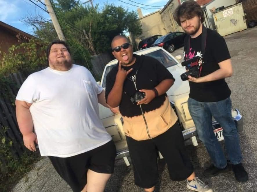 Three people standing outdoors in front of a car, smiling and posing for the photo.
