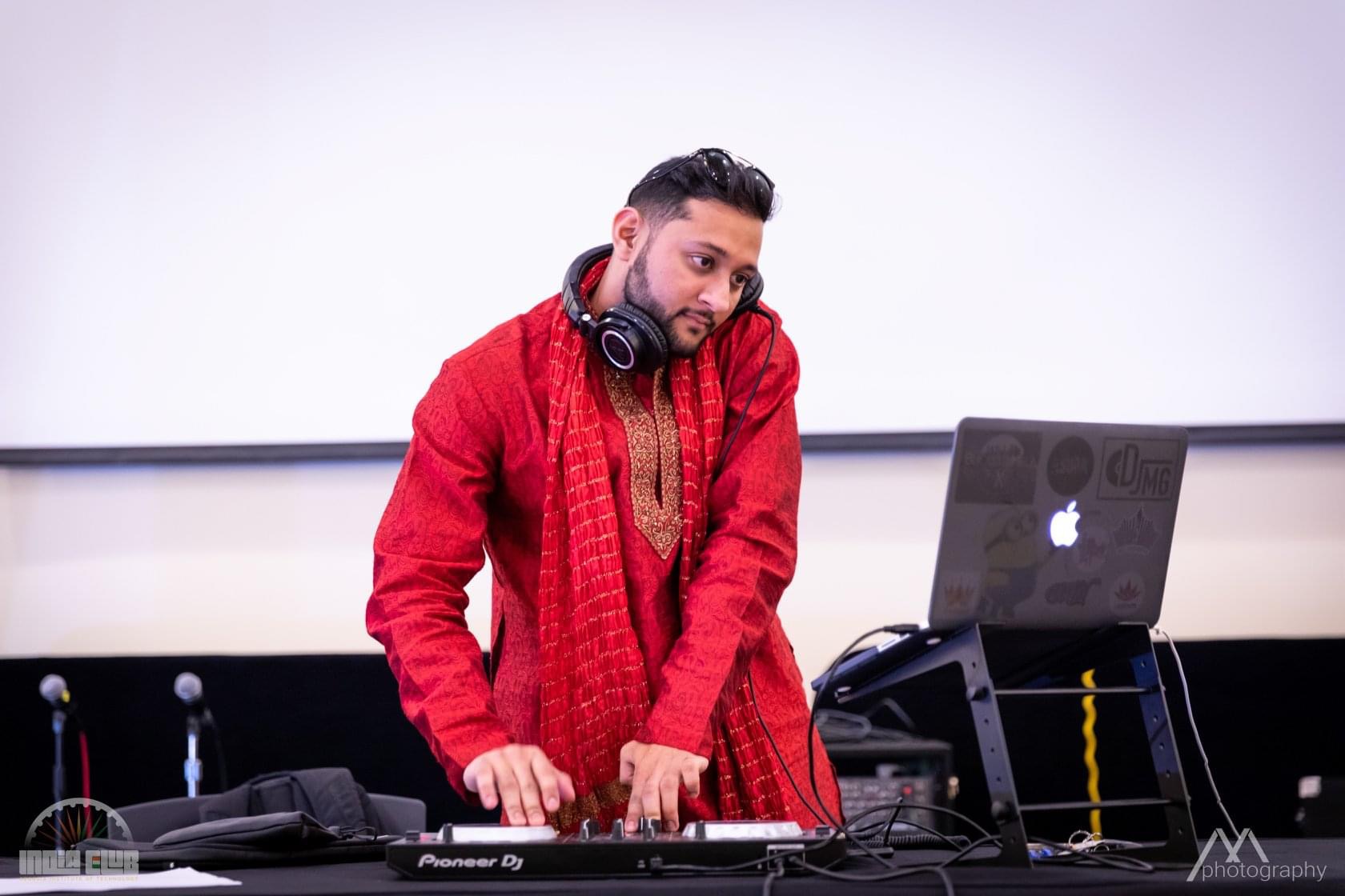 Man with headphones and a red sweater working at DJ equipment with a laptop, against a plain background.